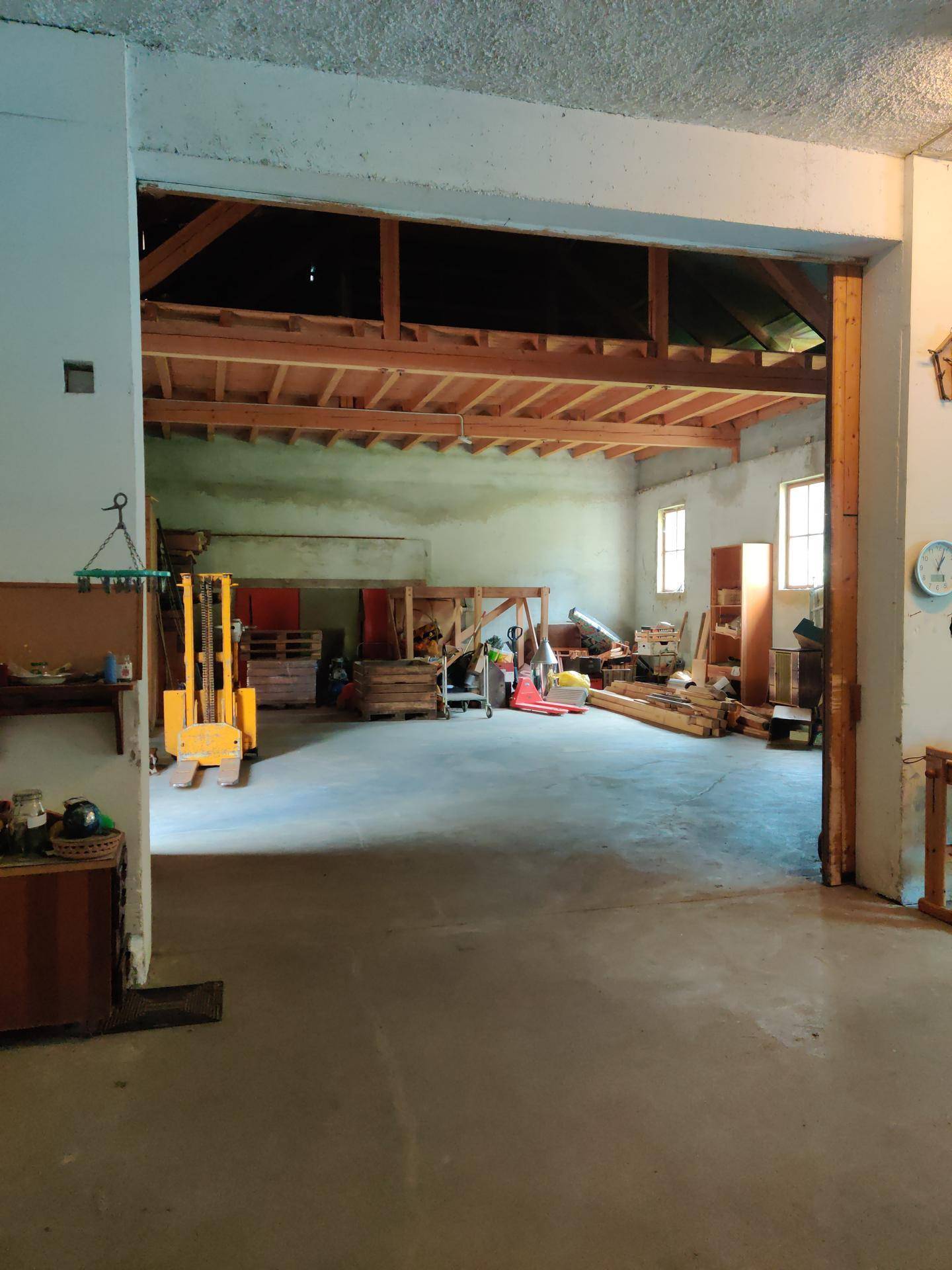 Großer, heller Werkstattraum mit Betonboden und sichtbarer Holzkonstruktion im Dachbereich.