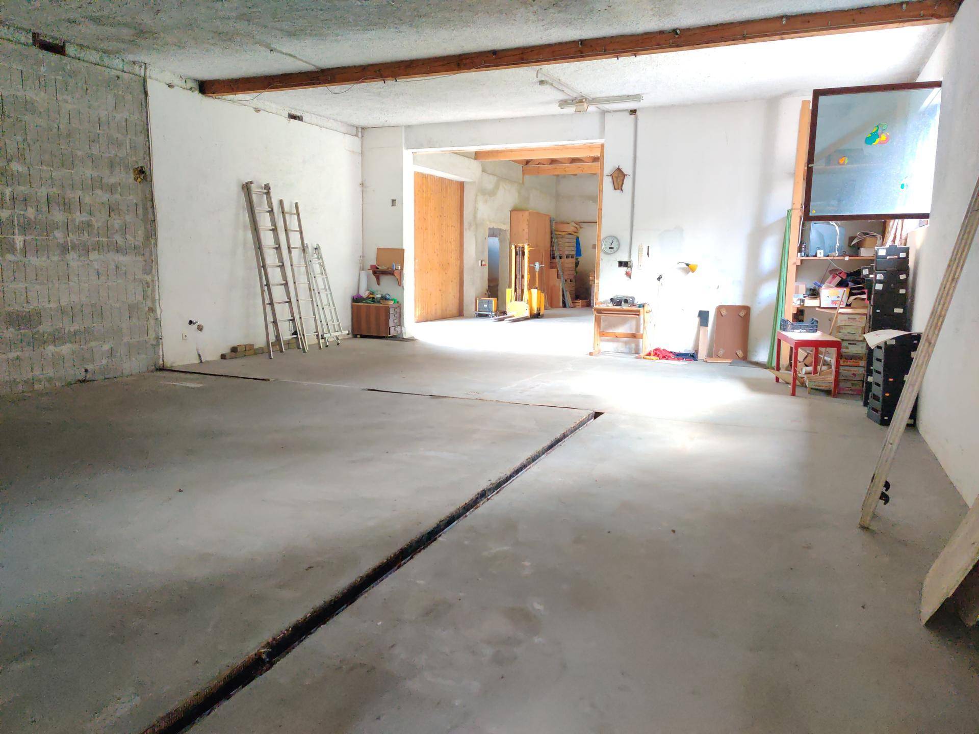 Großer, offener Raum mit Betonboden und sichtbaren Holzbalken, ideal für eine Werkstatt oder Lagerung.