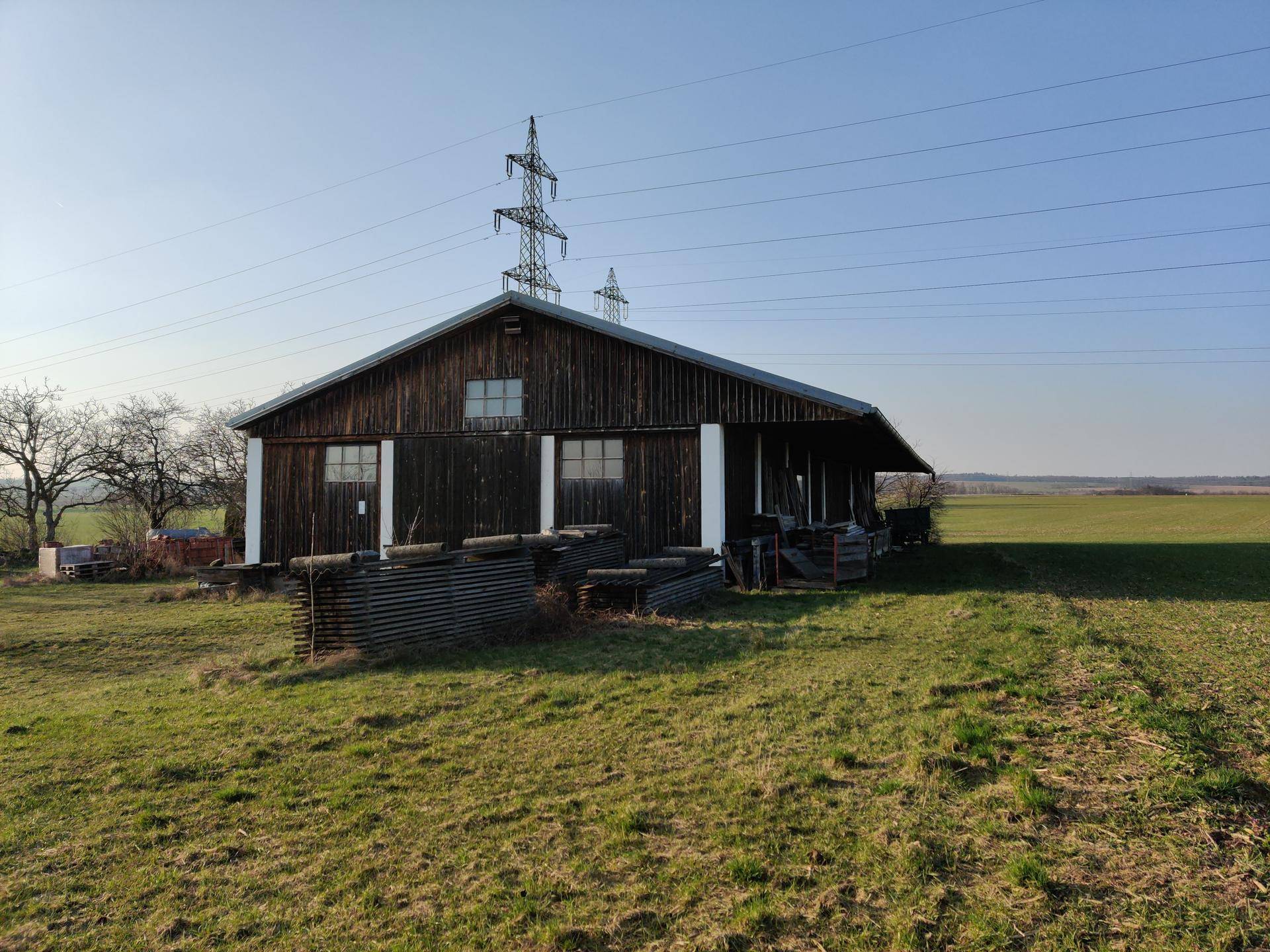 Rustikales Holzgebäude in einer weiten, grünen Landschaft unter einem klaren blauen Himmel.