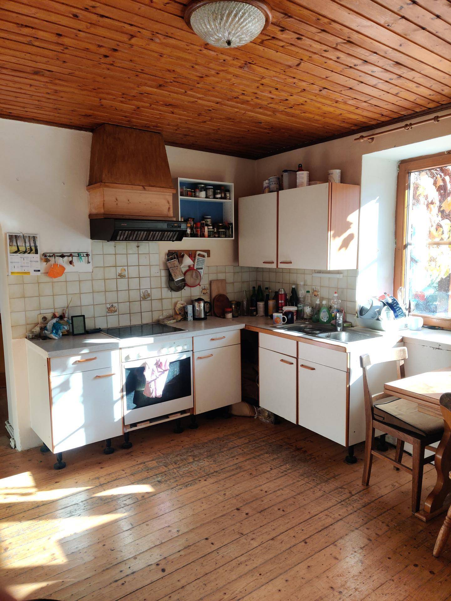 Funktionale Küche mit weißen Schränken, Holzdielenboden und einer Holzdecke.