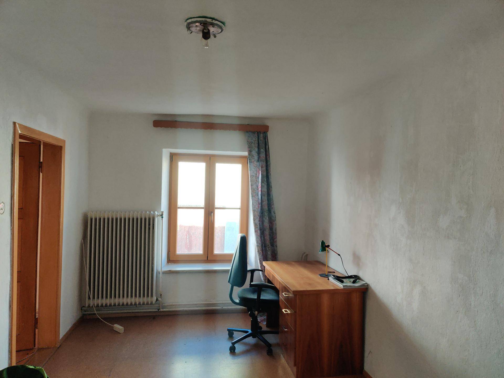 Einfaches Büro mit Schreibtisch, Stuhl und einem Fenster, das Tageslicht hereinlässt.