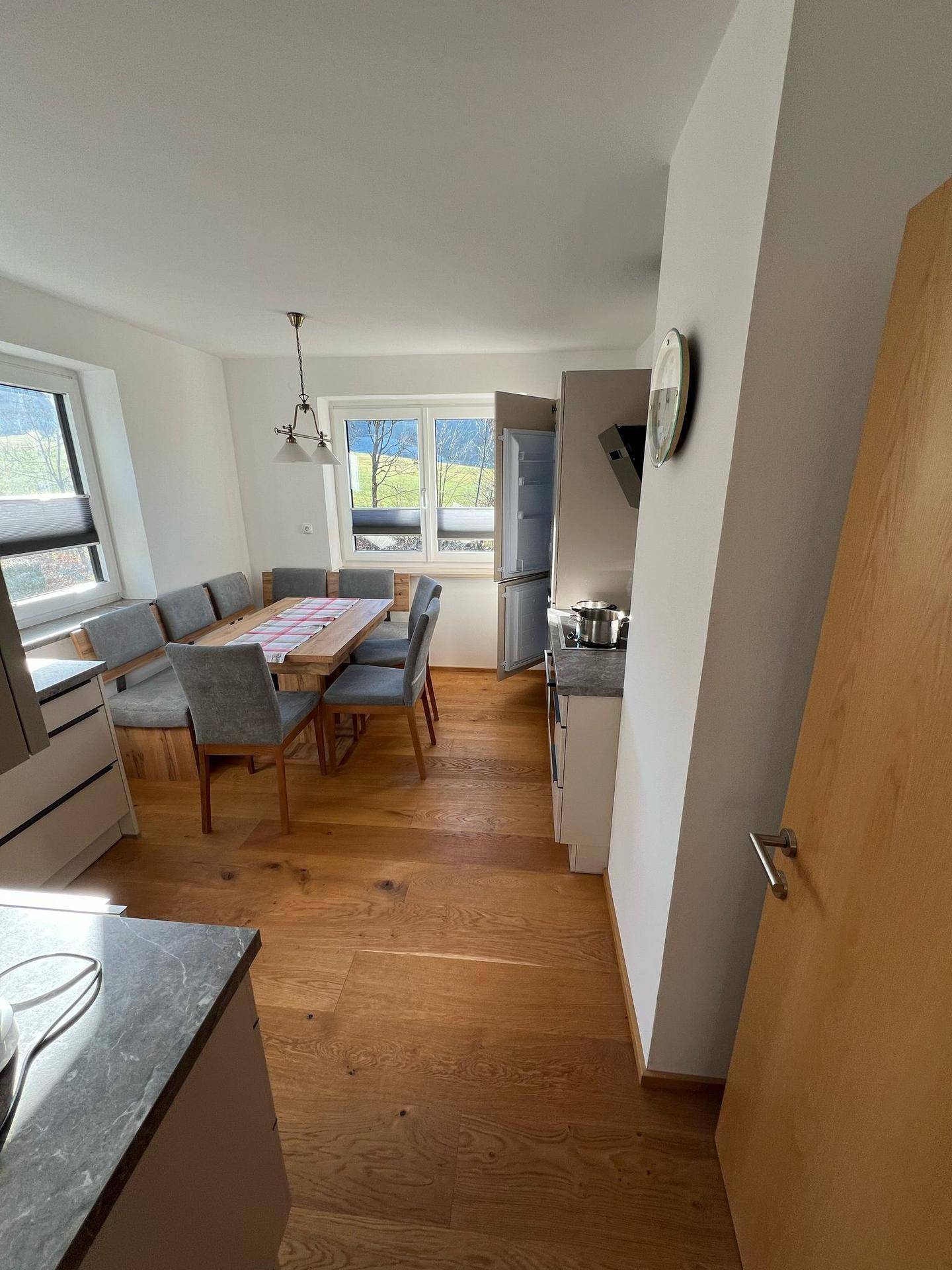 Helle Wohnküche mit Holzboden, integriertem Essbereich und weitem Blick ins Grüne durch große Fenster.