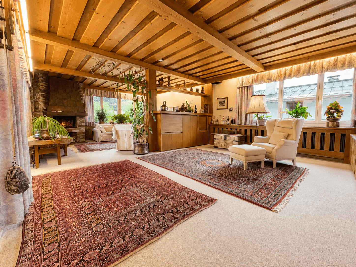 Gemütliches Wohnzimmer im alpinen Stil mit Holzbalkendecke, Kamin und traditionellen Teppichen.