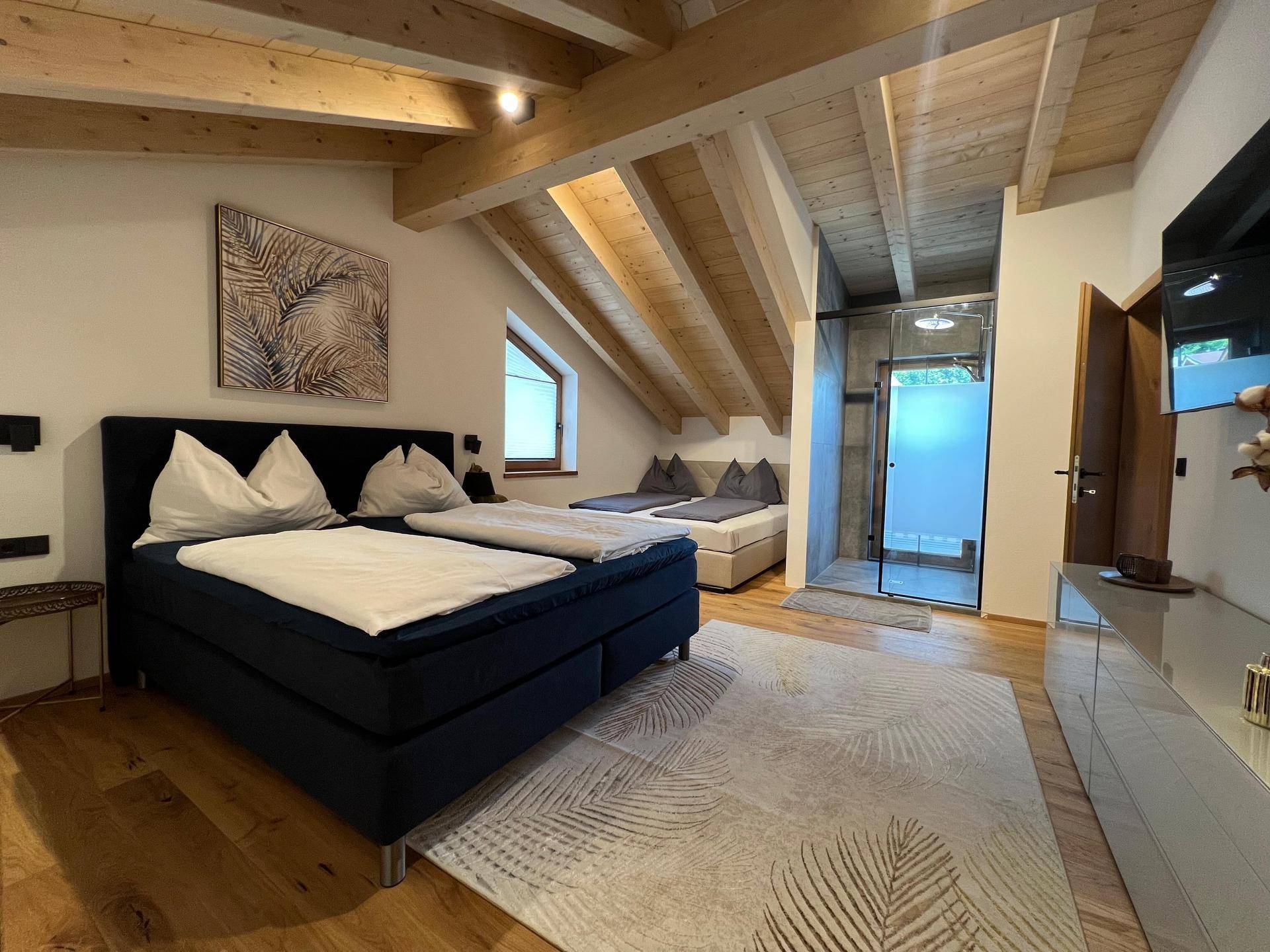 Helles Schlafzimmer im Dachgeschoss mit Holzbalken, Holzboden und integrierter begehbarer Dusche.