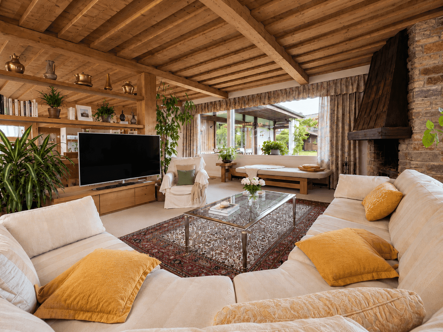 Helles Wohnzimmer mit großem Sofa, Fernseher und Blick ins Grüne durch die Fensterfront.