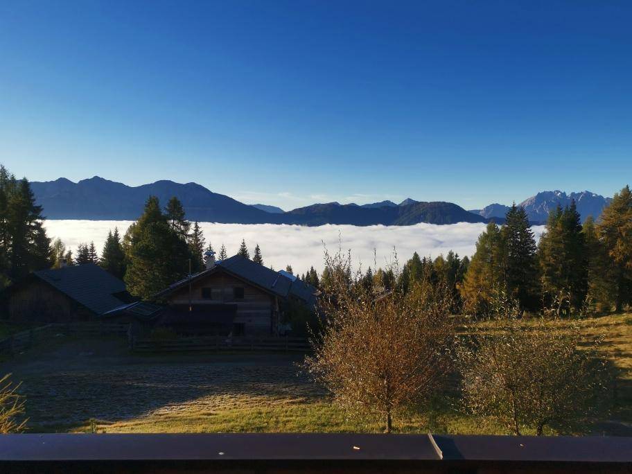 Panoramablick über die Wolken auf die umliegende Bergwelt und die Holzhäuser.