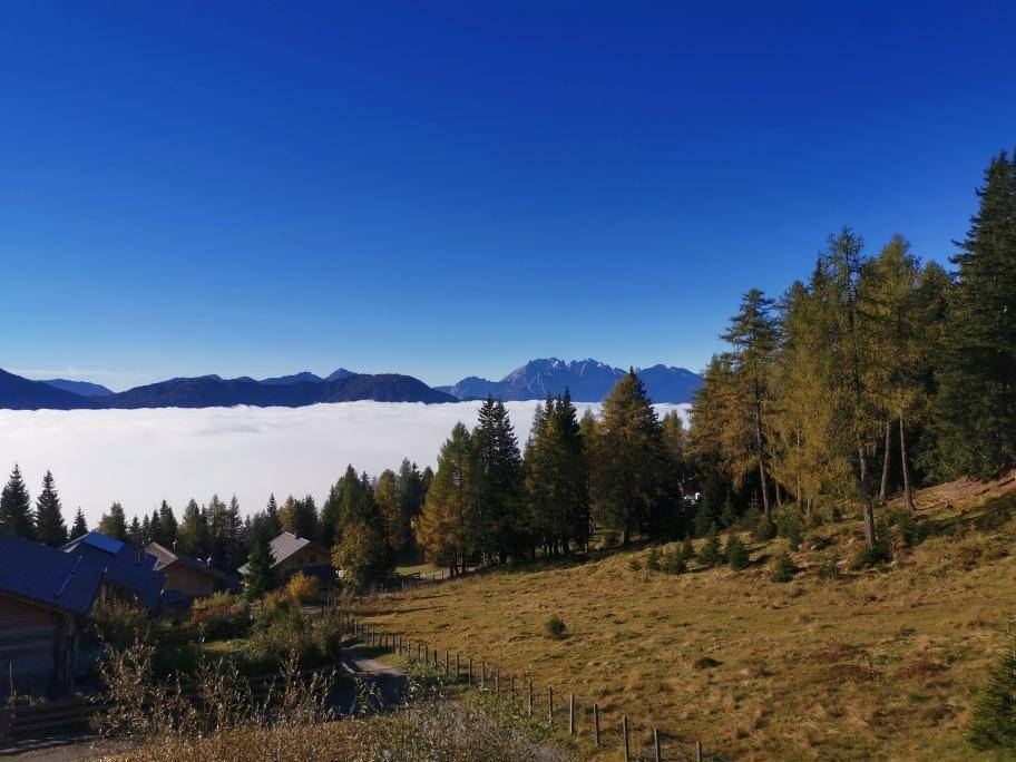Weitläufige alpine Landschaft mit verstreuten Holzhäusern und einem beeindruckenden Wolkenmeer.