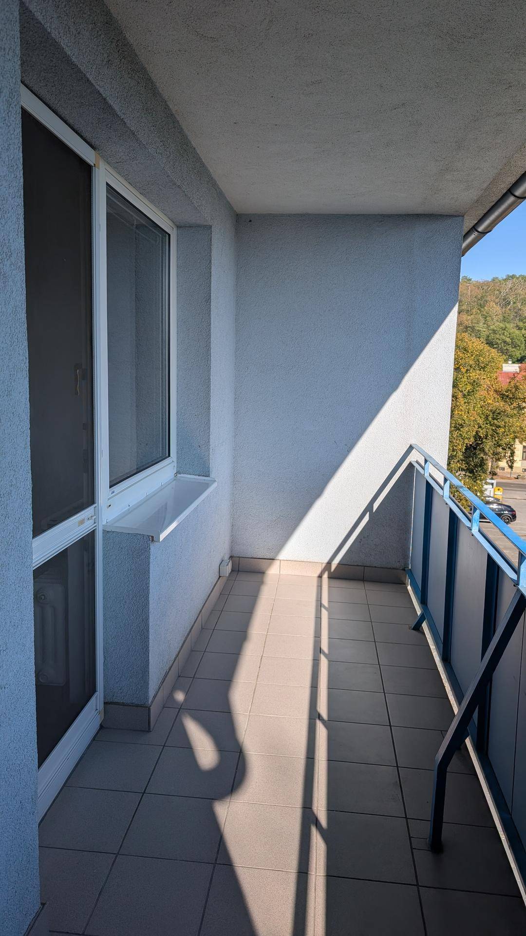 Schmaler Balkon mit Fliesenboden und blauem Geländer, sonnig beleuchtet.