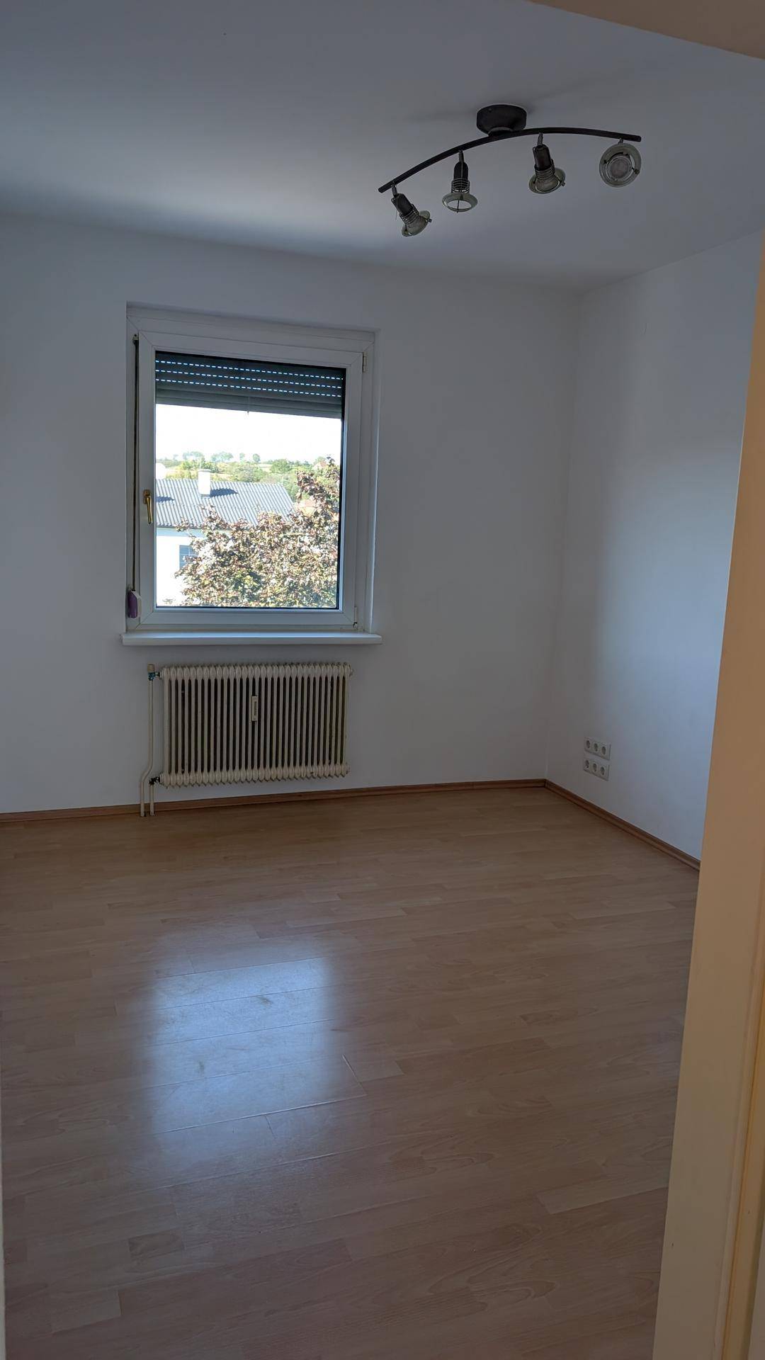 Helles Zimmer mit Laminatboden, Fenster und Blick ins Grüne.
