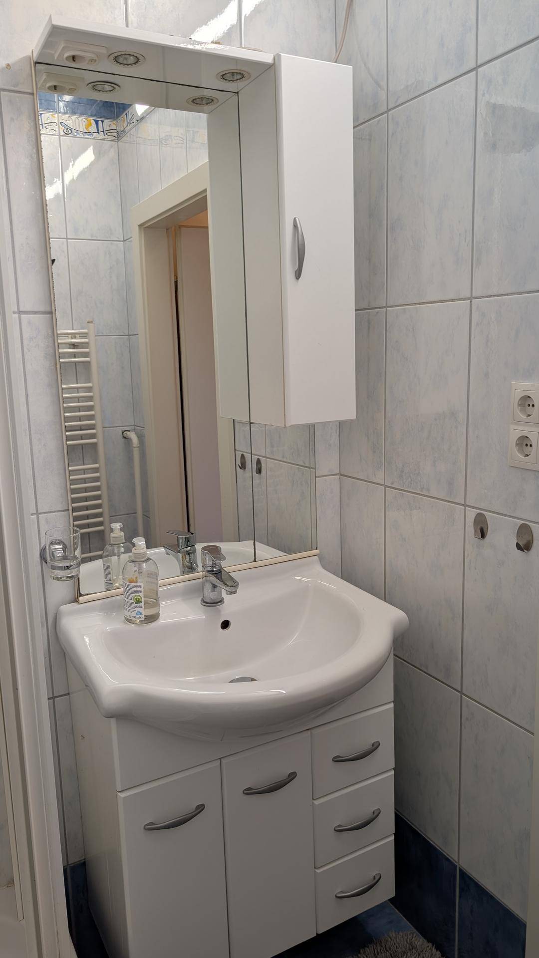Badezimmer mit Waschbecken, Spiegelschrank und hellblauen Fliesen an den Wänden.