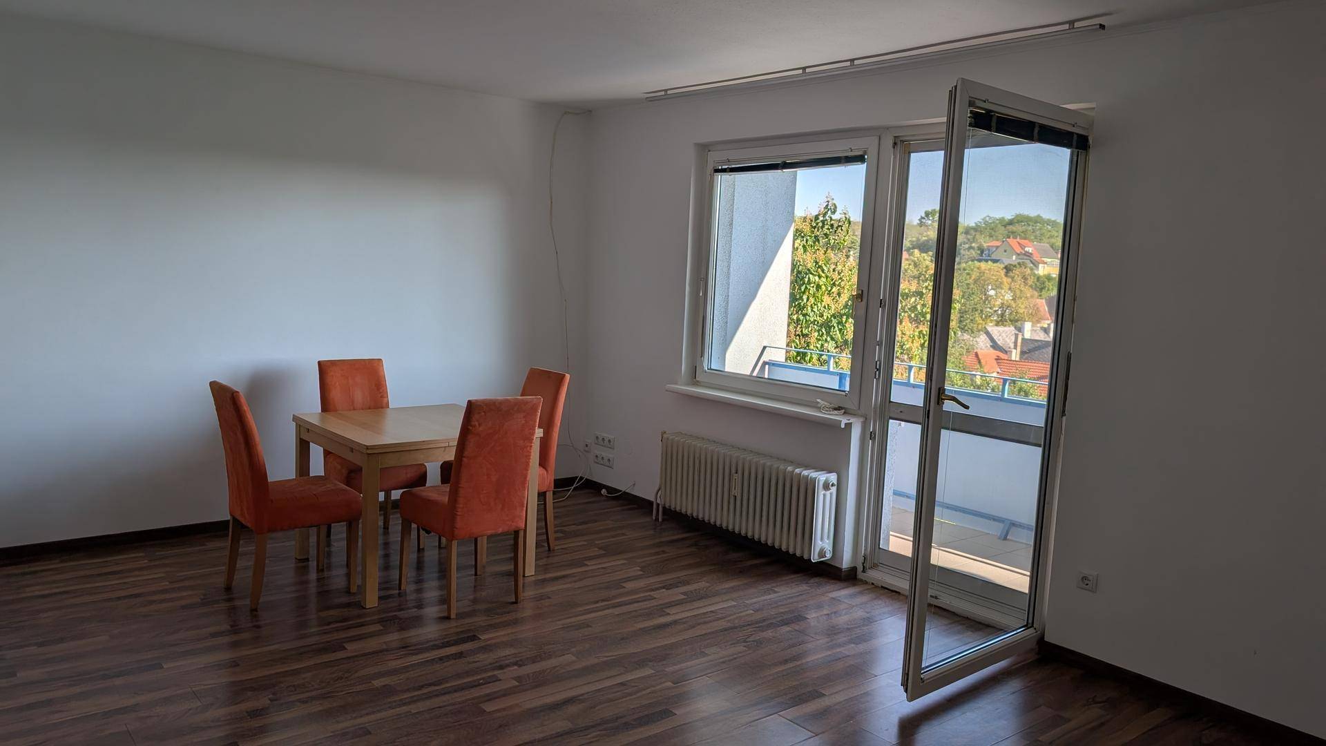 Wohnzimmer mit dunklem Laminatboden, Esstisch und Zugang zu einem sonnigen Balkon.