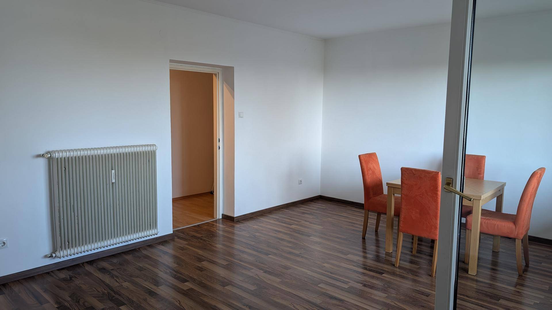 Wohnbereich mit Esstisch, dunklem Laminatboden und Heizkörper an der Wand.