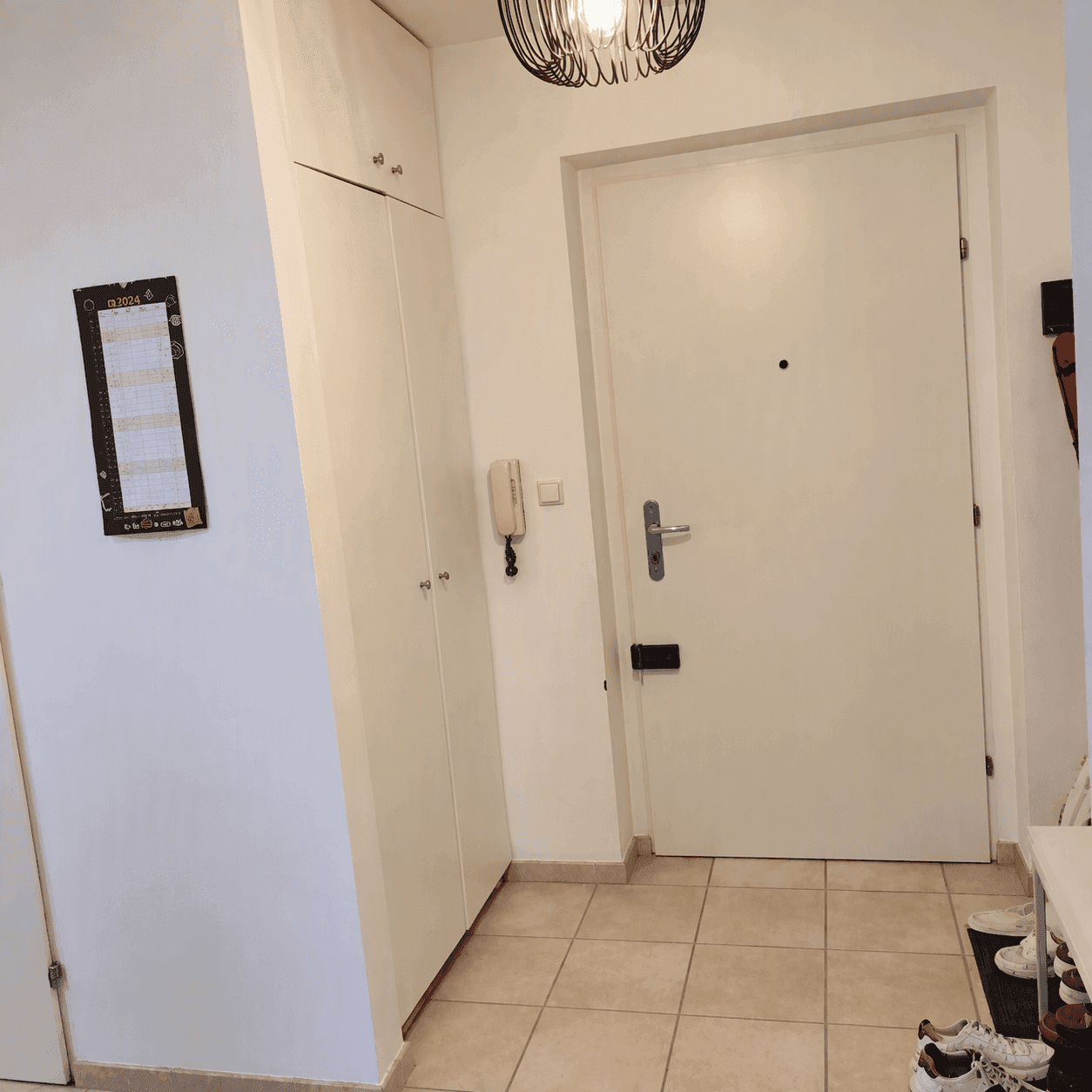 Eingangsbereich mit hellem Fliesenboden, weißem Einbauschrank und der Haustür.