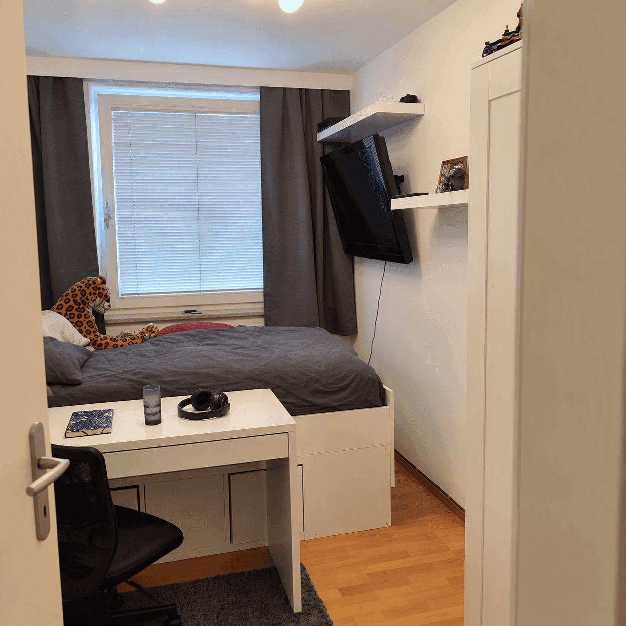 Gemütliches Schlafzimmer mit Einzelbett, Schreibtisch und einem Fenster mit Jalousien.