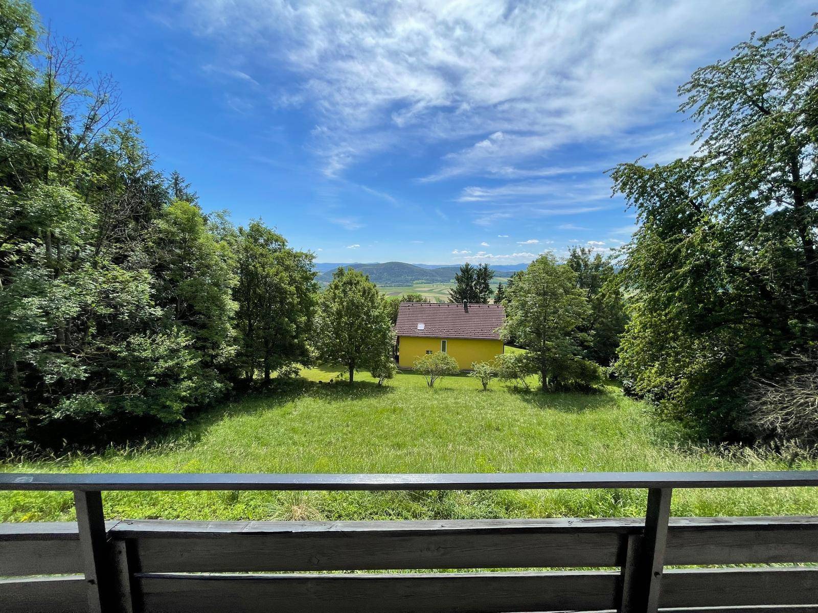 Malerischer Ausblick von der Terrasse auf eine weite grüne Landschaft mit einem gelben Haus.