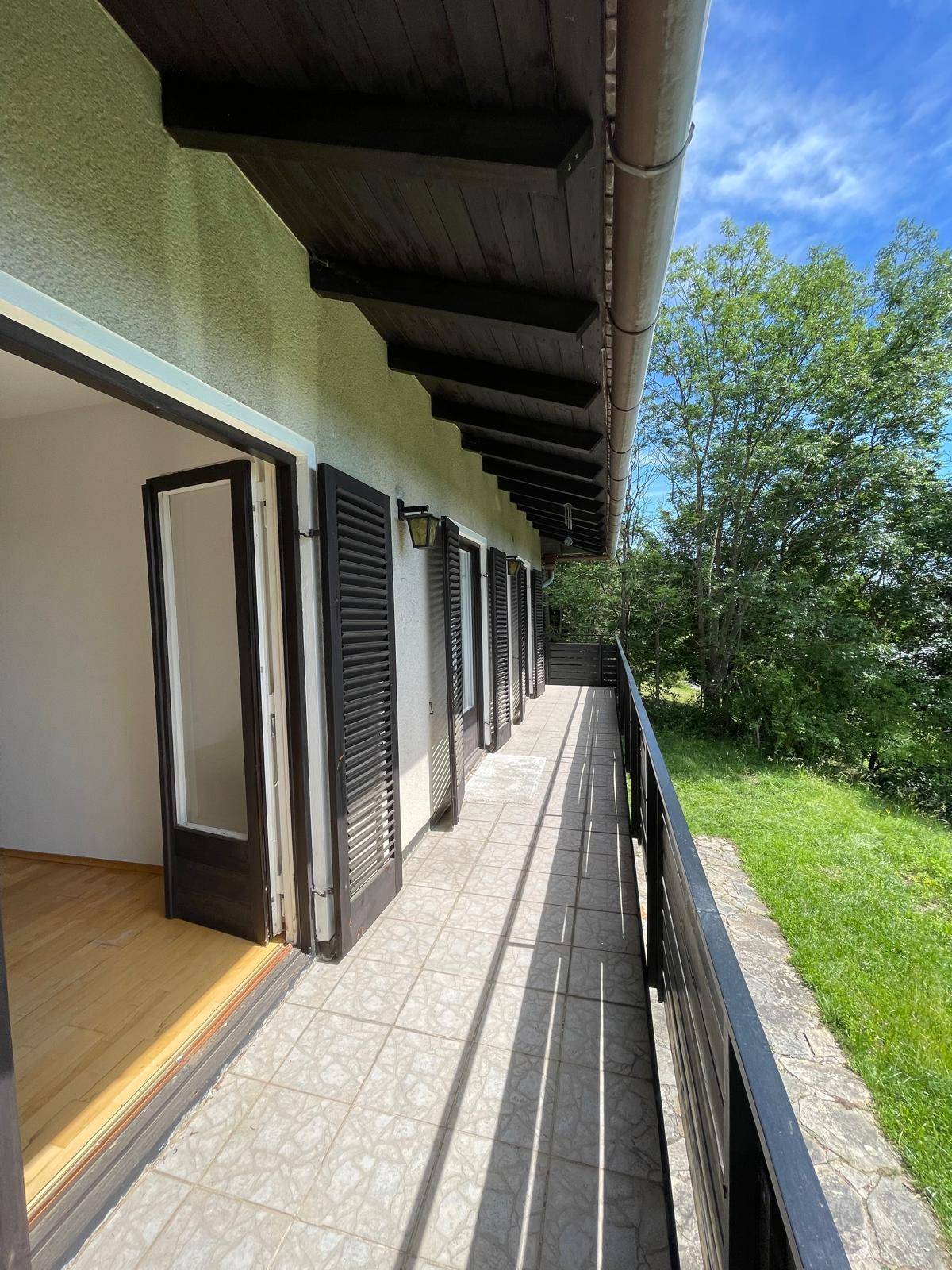 Langer Balkon mit Fliesenboden und Holzgeländer, zugänglich von mehreren Zimmern.