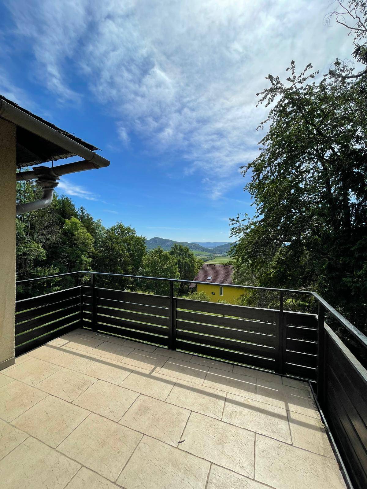 Geräumiger Balkon mit Fliesenboden und weitem Panoramablick über die grüne Landschaft.