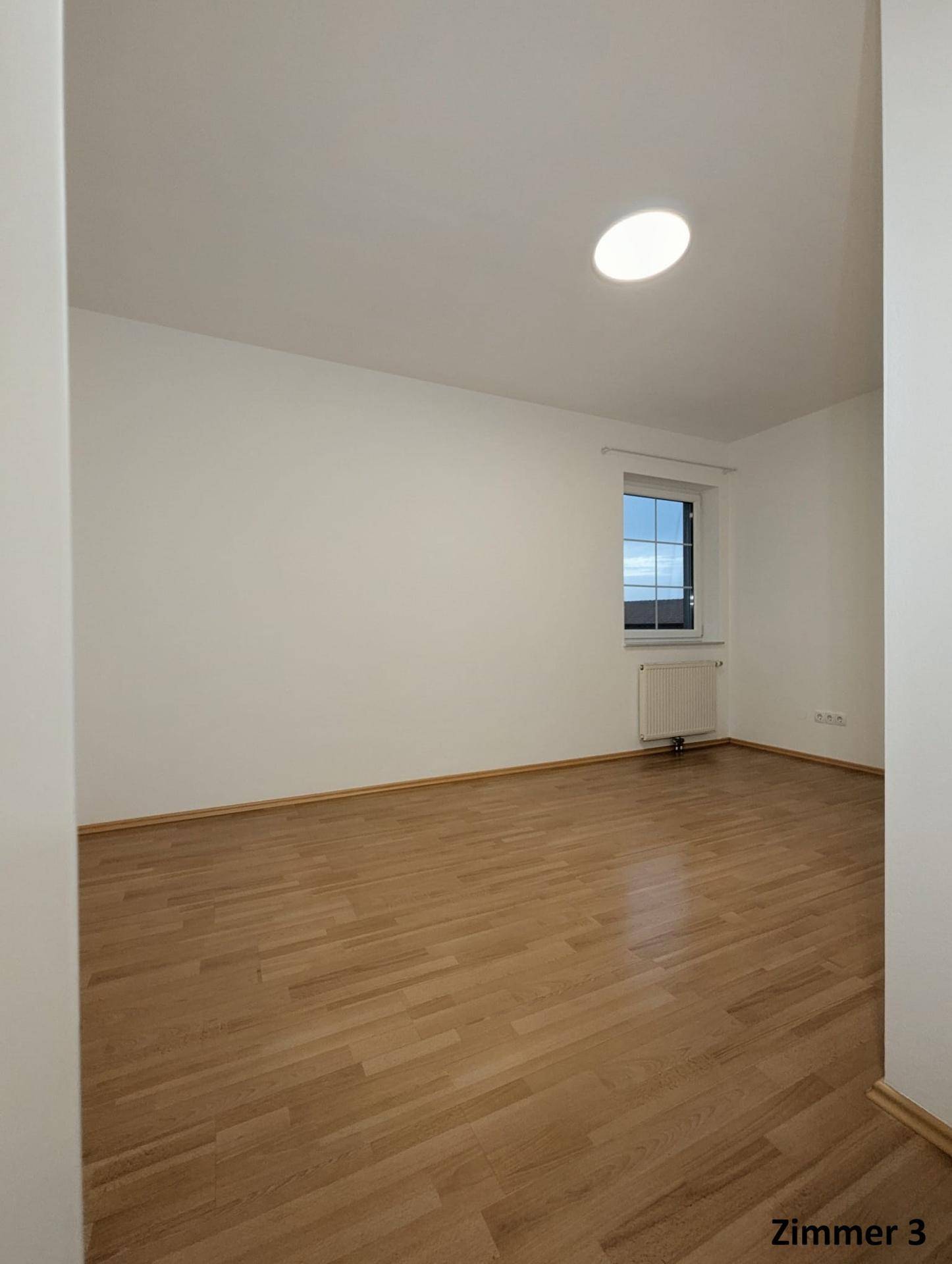 Helles Zimmer mit Parkettboden, weißen Wänden und einem Fenster, ideal als Schlaf- oder Gästezimmer.