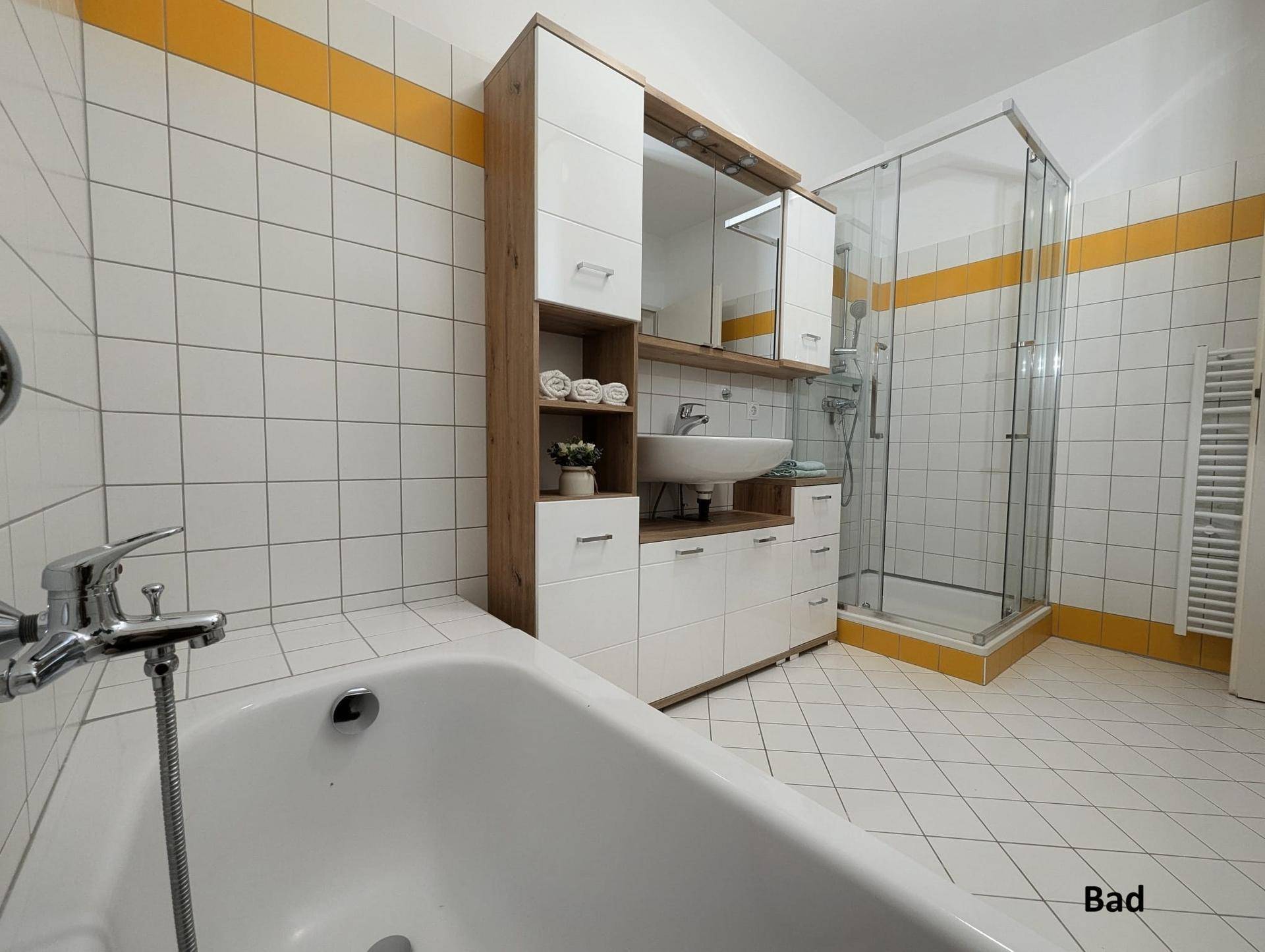 Badezimmer mit Badewanne, Duschkabine und modernem Waschtisch, akzentuiert mit gelben Fliesen.