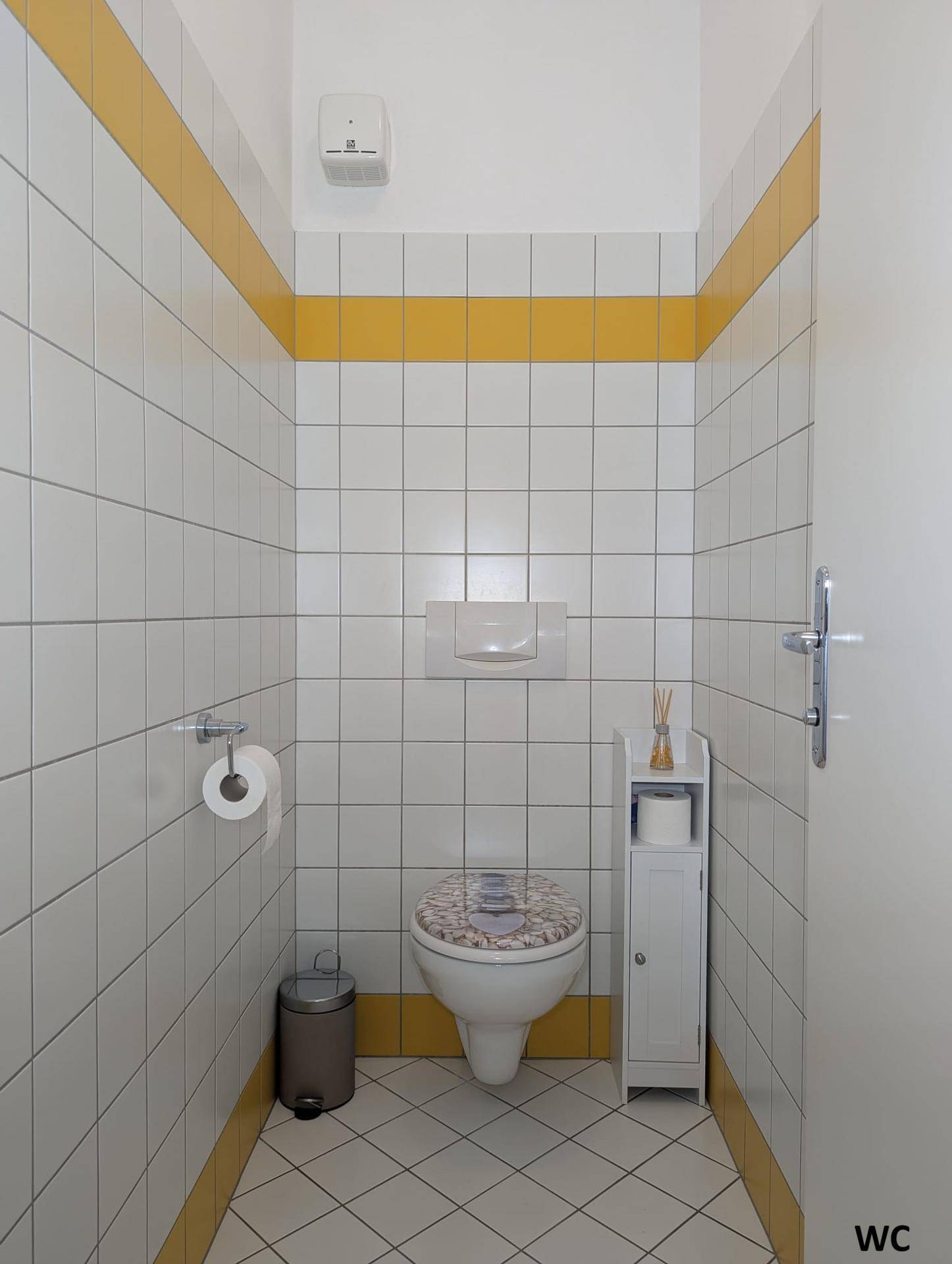Kleines Gäste-WC mit weißen Fliesen, gelben Akzentstreifen und wandhängendem WC.