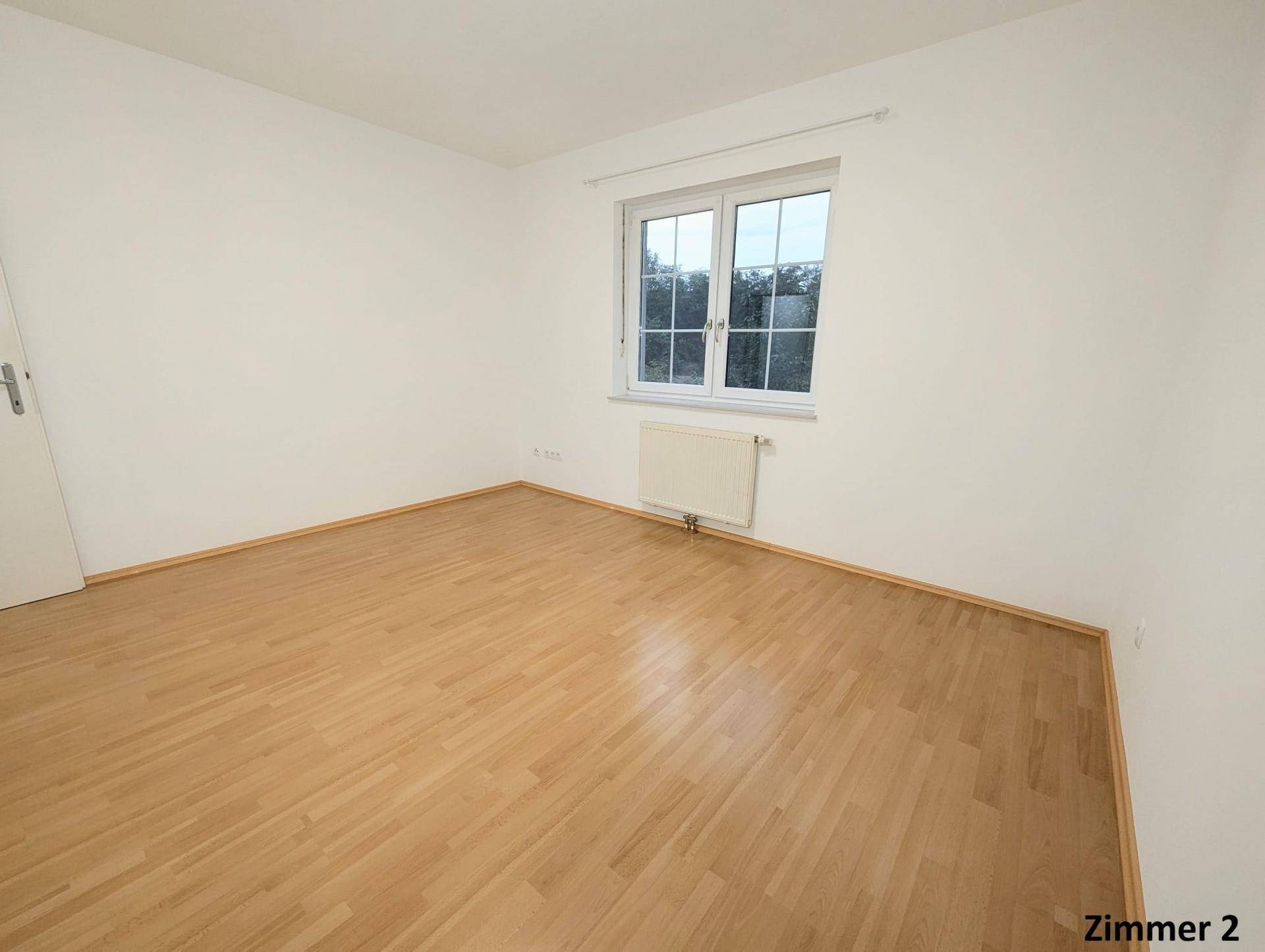 Helles Zimmer mit Holzboden und Fenster, das einen Blick nach draußen bietet.