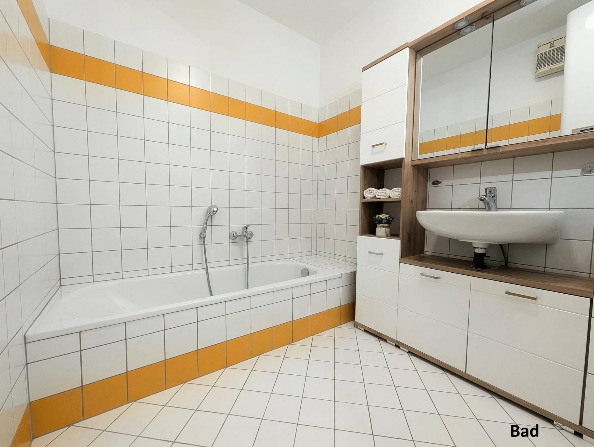 Badezimmer mit Badewanne, Waschbecken und Spiegelschrank, dekoriert mit gelben Fliesenstreifen.