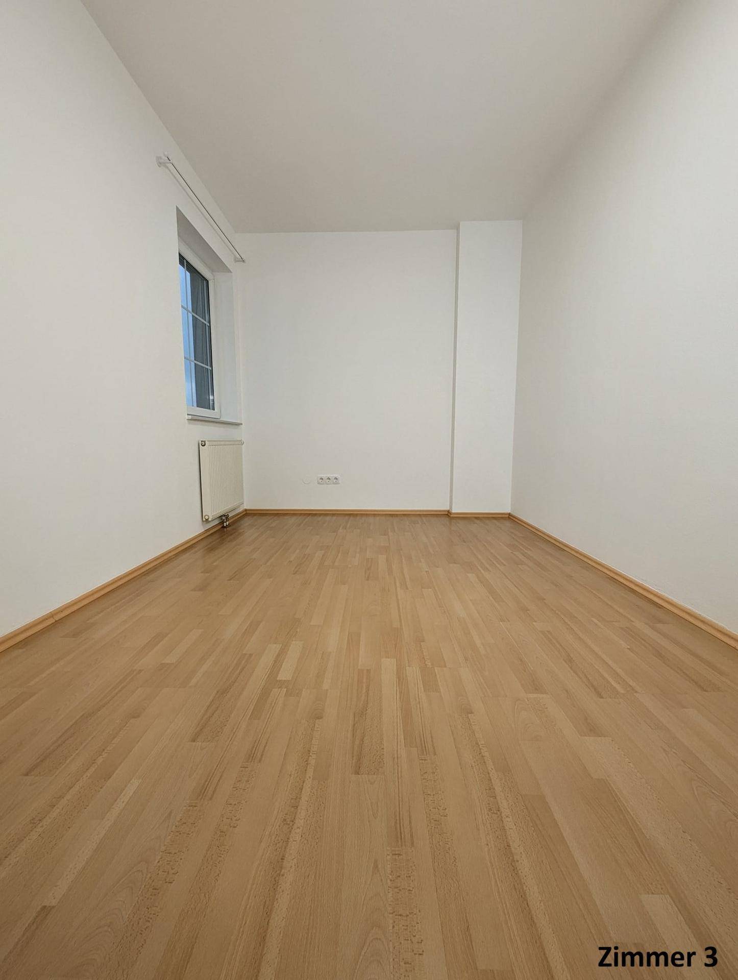 Helles Zimmer mit Holzboden und Fenster, das viel natürliches Licht in den Raum bringt.