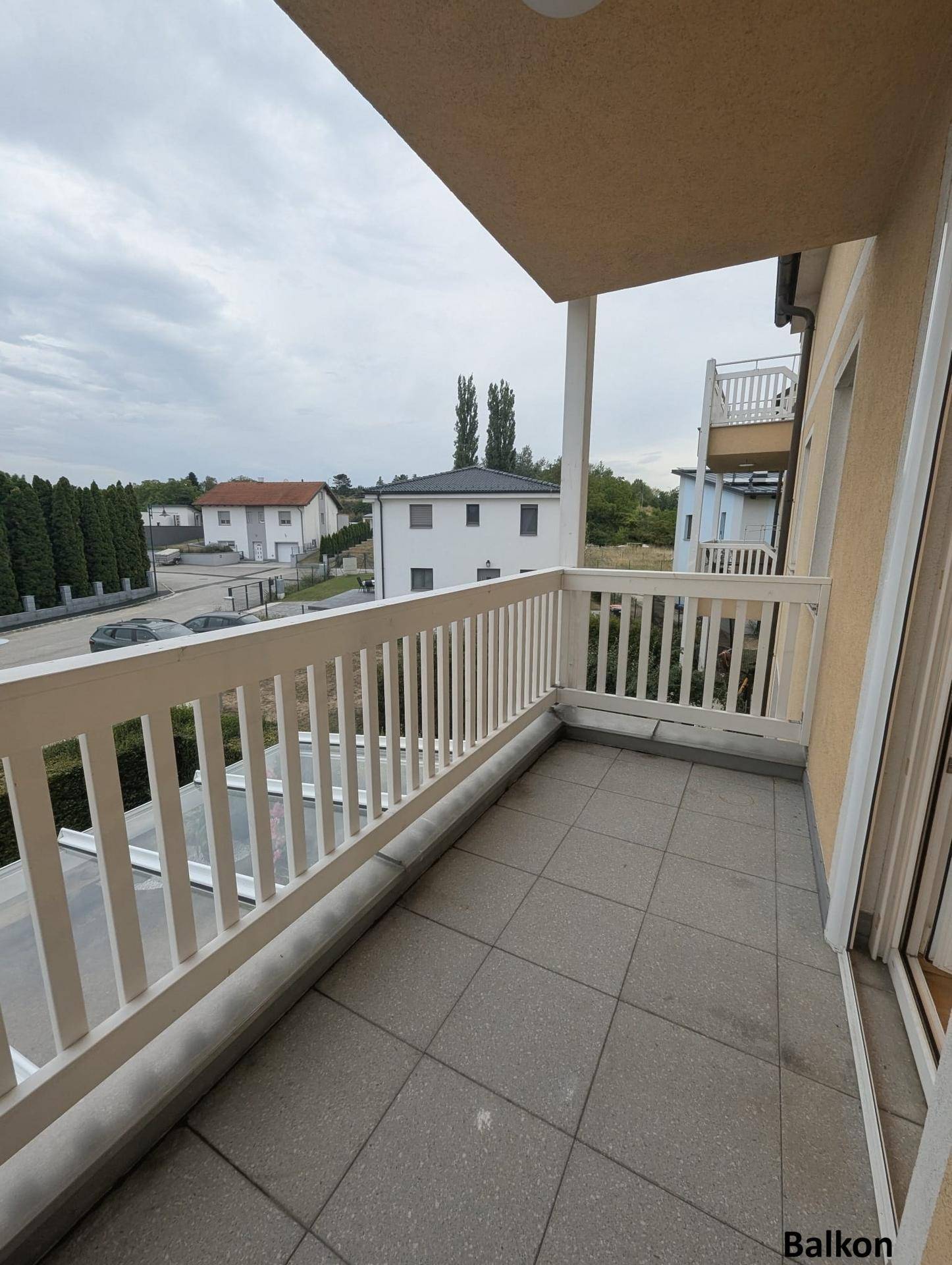 Heller Balkon mit Fliesenboden und Blick auf die umliegende Wohngegend und Bäume.