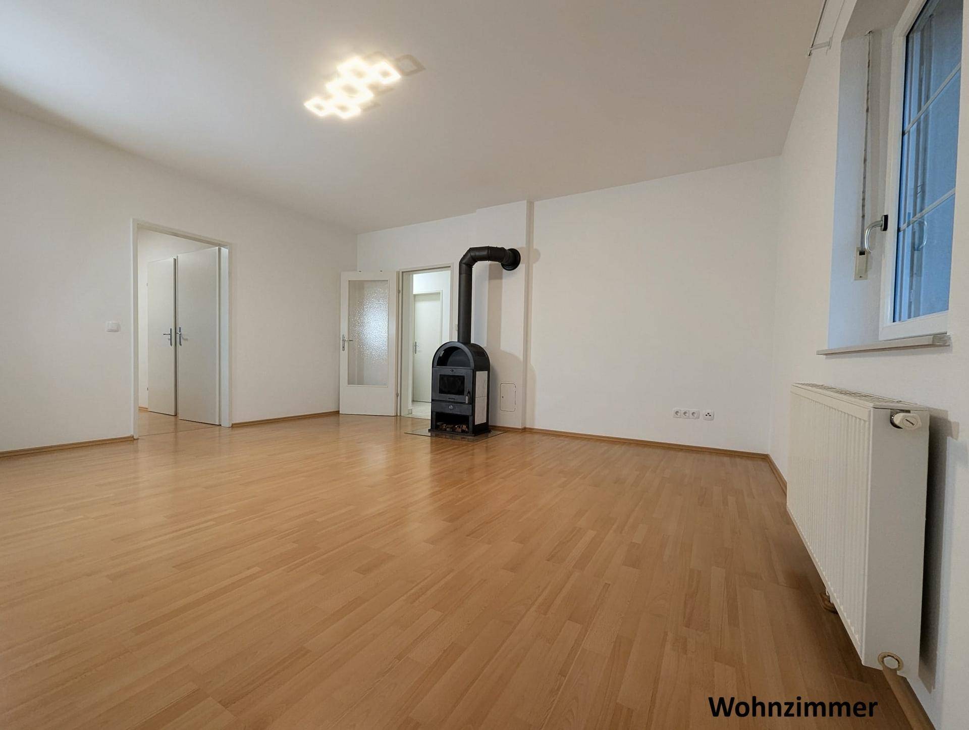 Geräumiges Wohnzimmer mit Parkettboden und einem gemütlichen Holzofen als zentrale Wärmequelle.