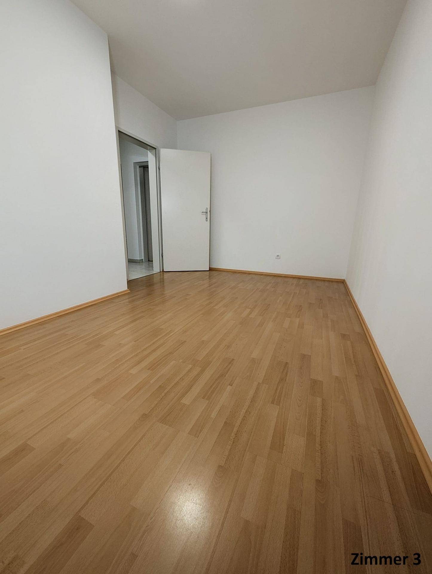 Leeres Zimmer mit Holzboden und weiß gestrichenen Wänden, bereit zur individuellen Einrichtung.