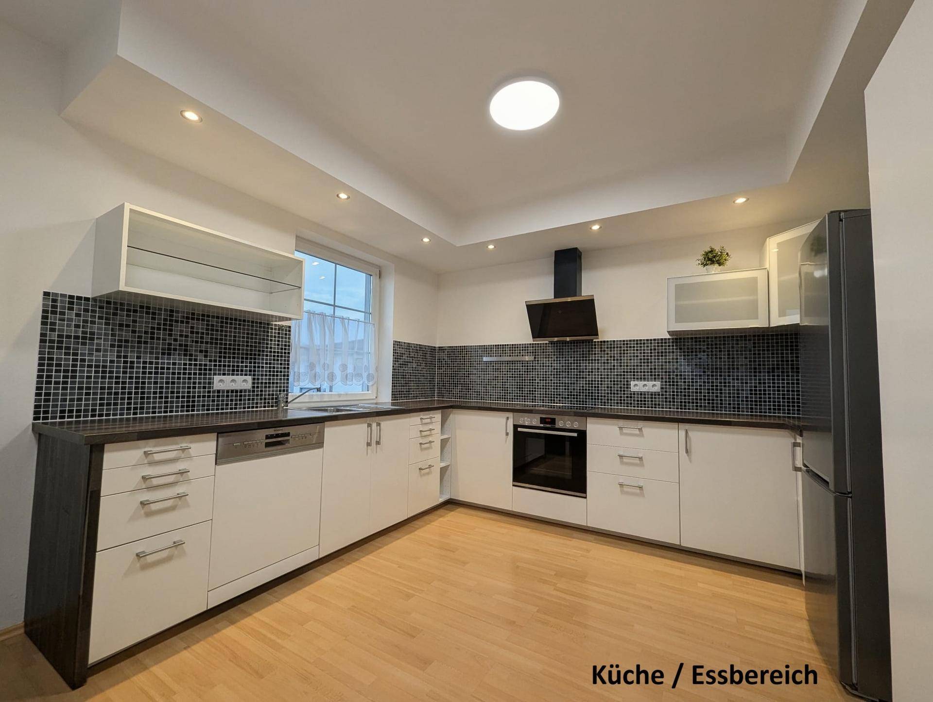 Moderne Einbauküche mit weißen Schränken, dunkler Arbeitsplatte und integrierten Geräten.