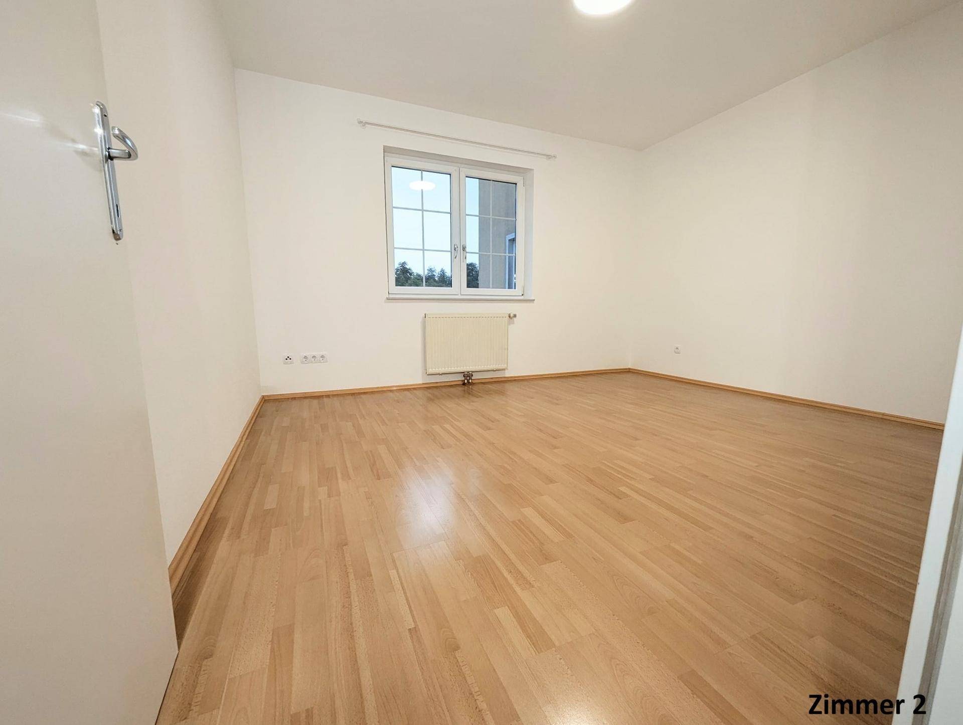 Geräumiges Zimmer mit Holzboden und weiß gestrichenen Wänden, ideal als Schlafzimmer.