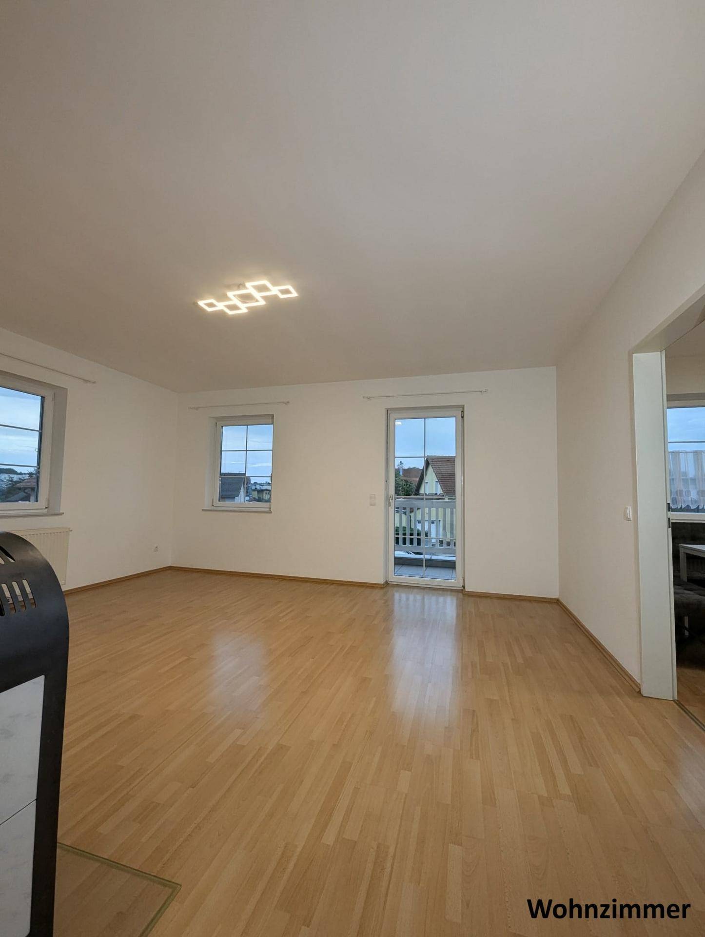 Lichtdurchflutetes Wohnzimmer mit Parkettboden, Balkonzugang und einem stilvollen Holzofen.