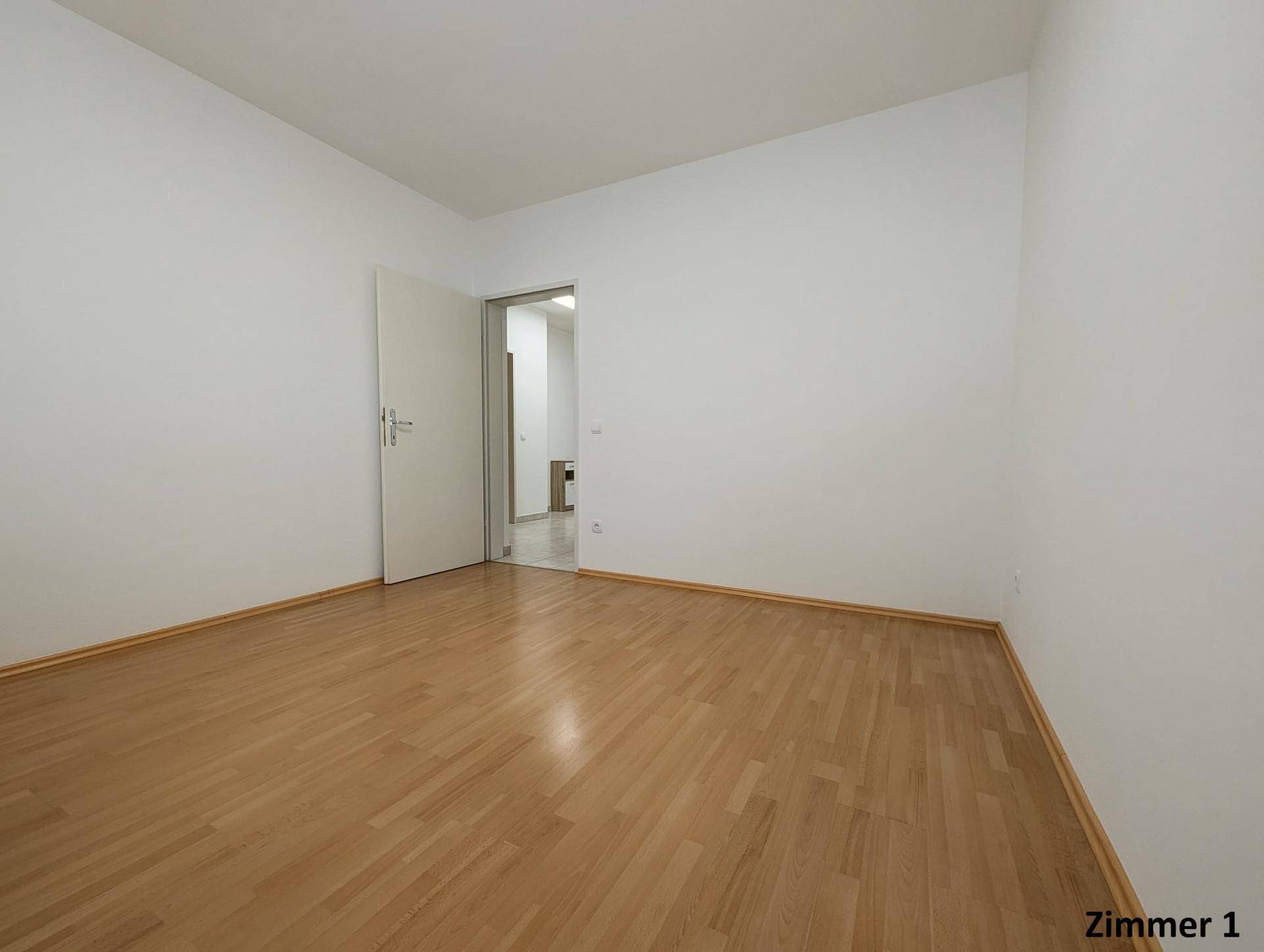 Leeres Zimmer mit Holzboden und weiß gestrichenen Wänden, bereit zur individuellen Gestaltung.