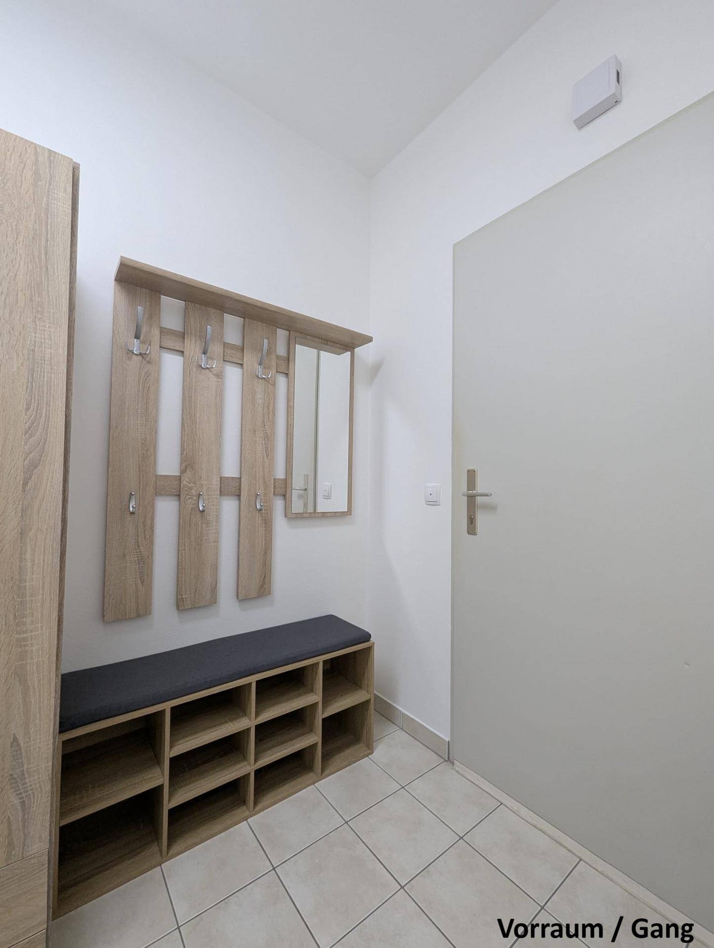 Heller Eingangsbereich mit Fliesenboden, Garderobe und Schuhregal in Holzoptik.