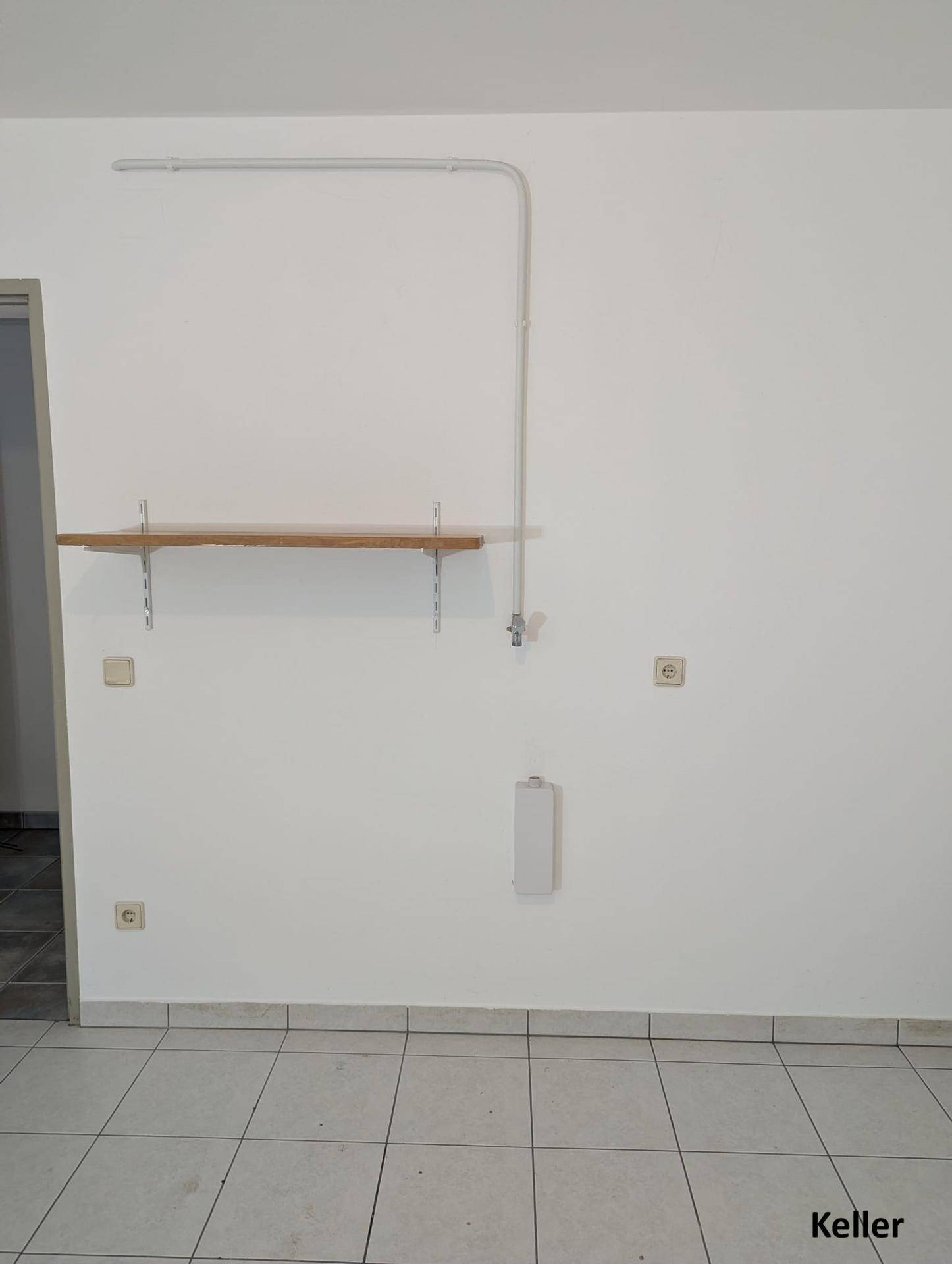 Kellerraum mit Fliesenboden, Regal und sichtbaren Installationen an der Wand.