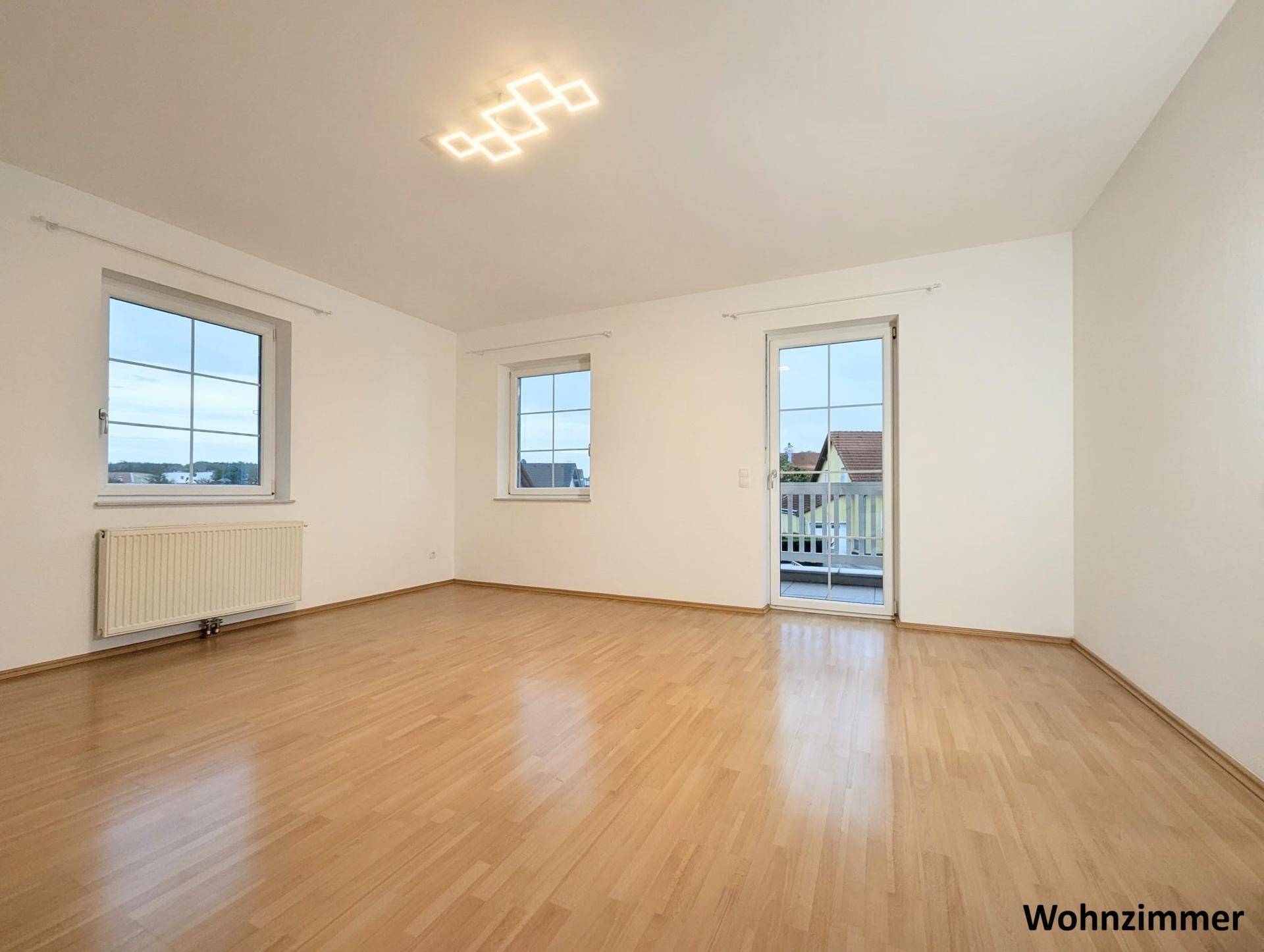 Großes, helles Wohnzimmer mit Parkettboden, modernen Deckenleuchten und Zugang zum Balkon.
