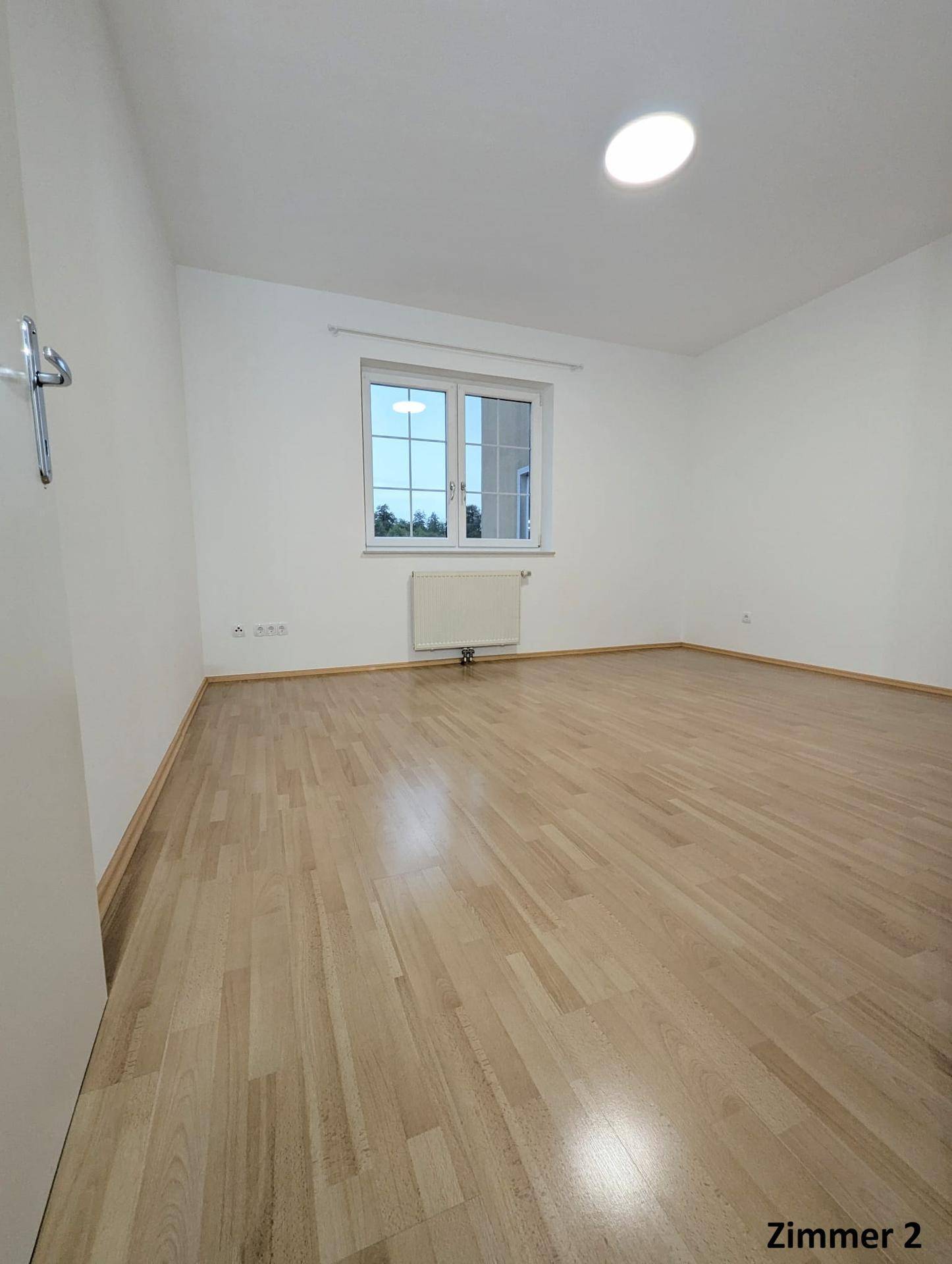 Freundliches Zimmer mit Holzboden und großem Fenster, das viel Tageslicht hereinlässt.