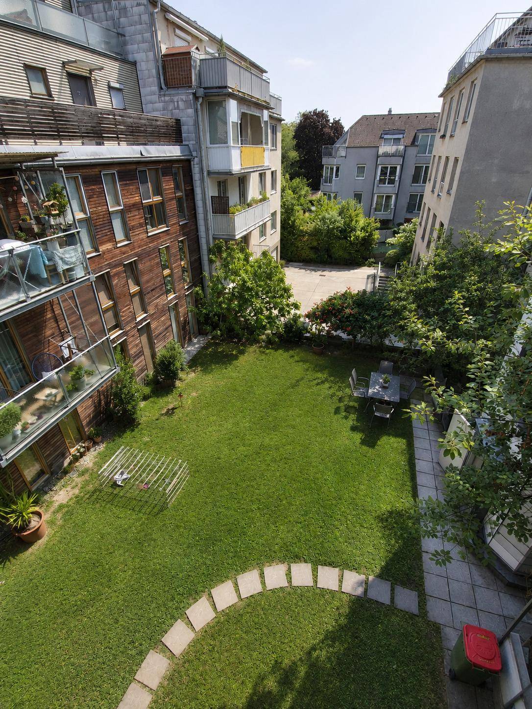 Gepflegter Gemeinschaftsgarten mit Rasenfläche, Sitzbereich und umliegenden Gebäuden.