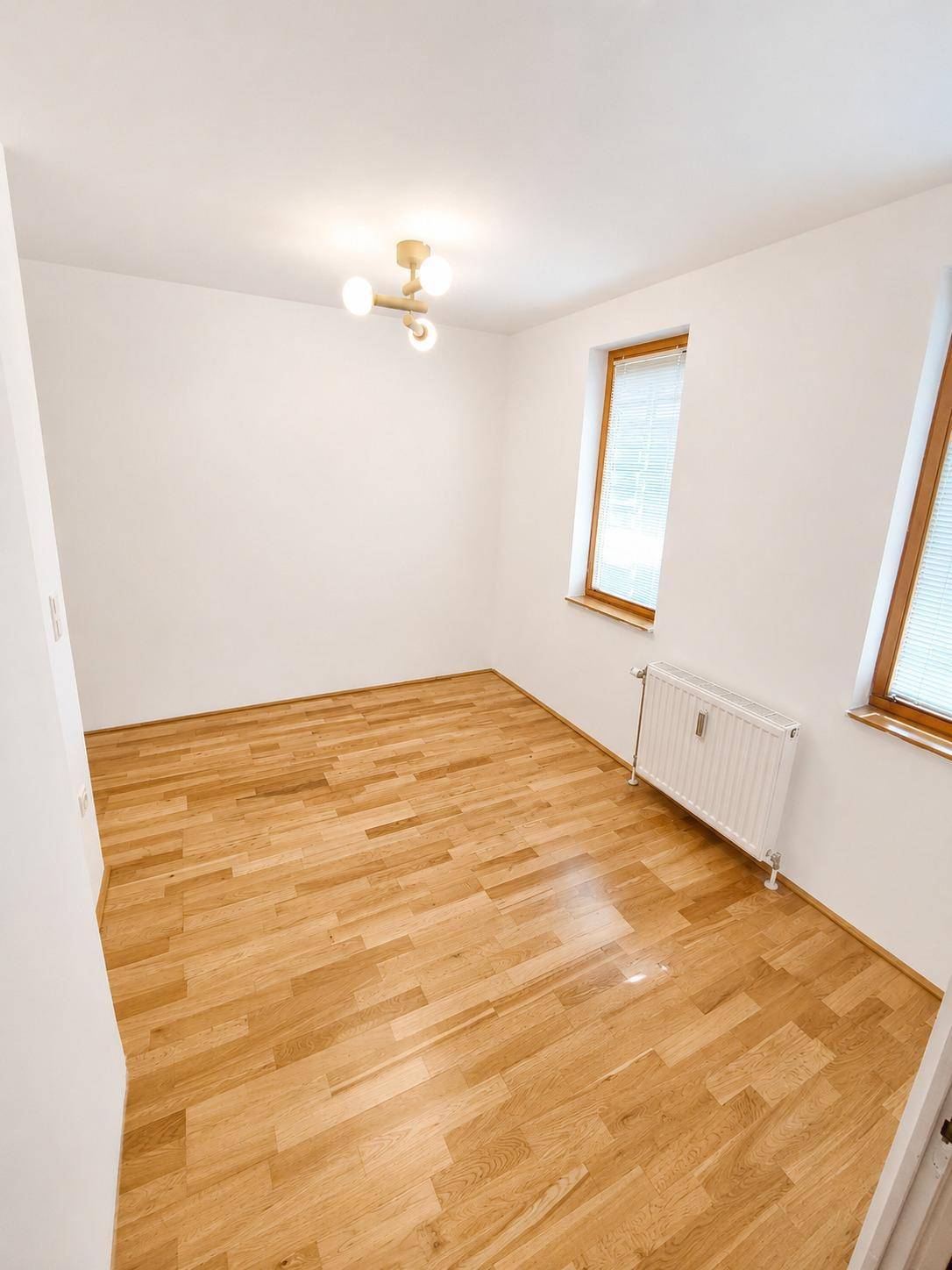 Ruhiges Schlafzimmer mit hellem Parkettboden und viel Tageslicht durch die Fenster.