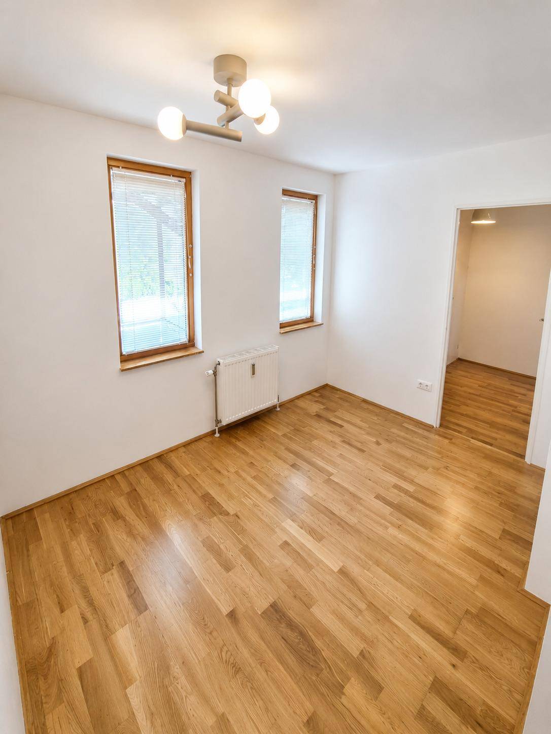 Helles Schlafzimmer mit Parkettboden und zwei Fenstern mit Blick ins Grüne.