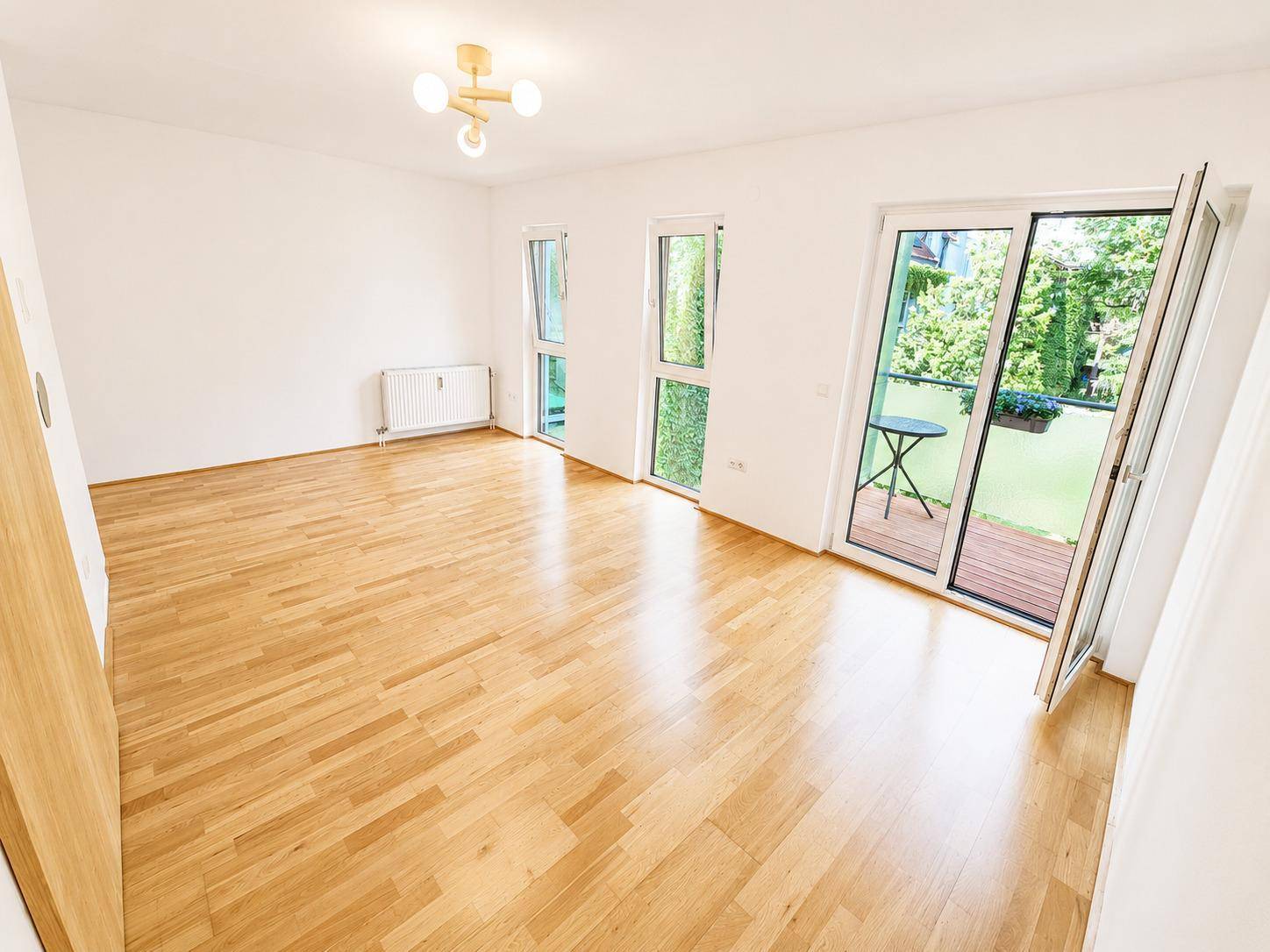 Geräumiges Wohnzimmer mit hellem Parkettboden und Blick auf die grüne Umgebung.