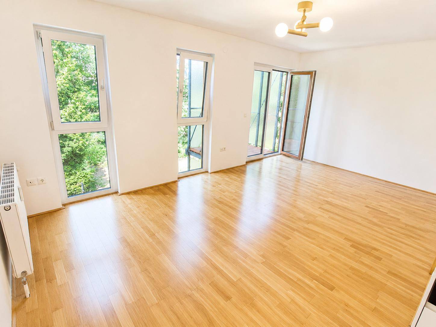 Helles Wohnzimmer mit Parkettboden, großen Fenstern und Zugang zur Loggia.