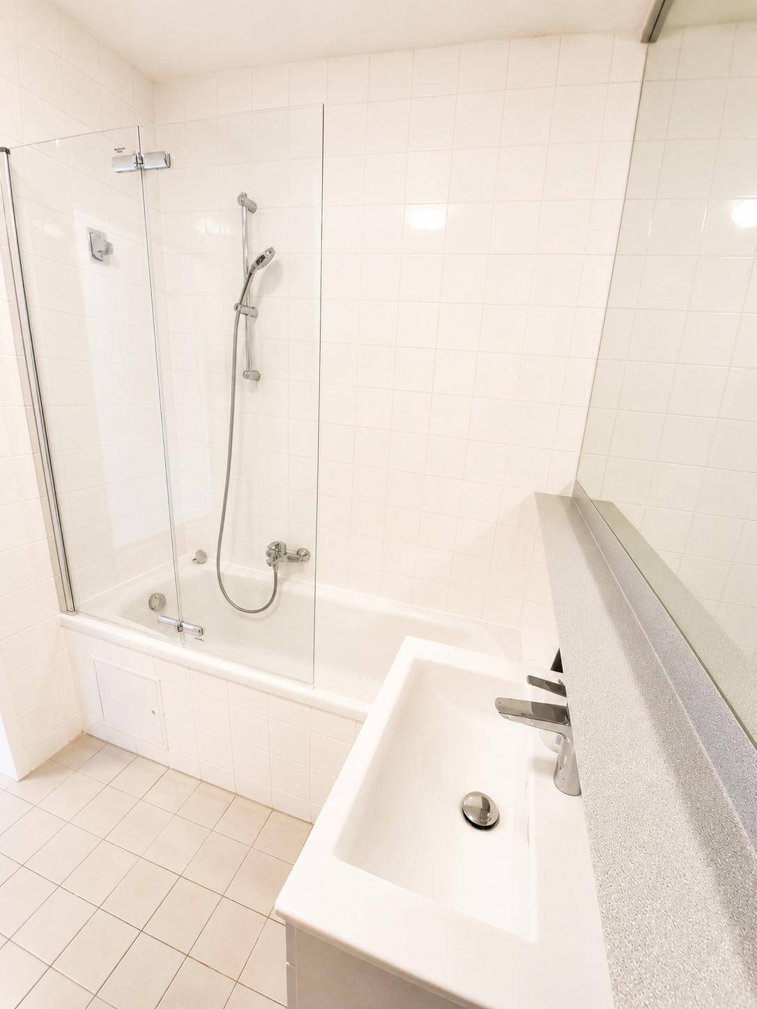 Badezimmer mit Badewanne und Duschabtrennung, Waschtisch und großem Spiegel.