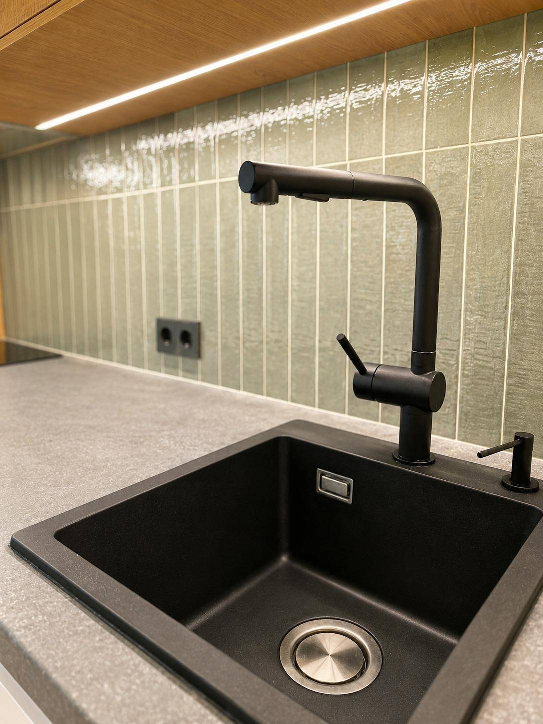 Schwarze Spüle mit modernem Wasserhahn und grauer Arbeitsplatte in der Küche.