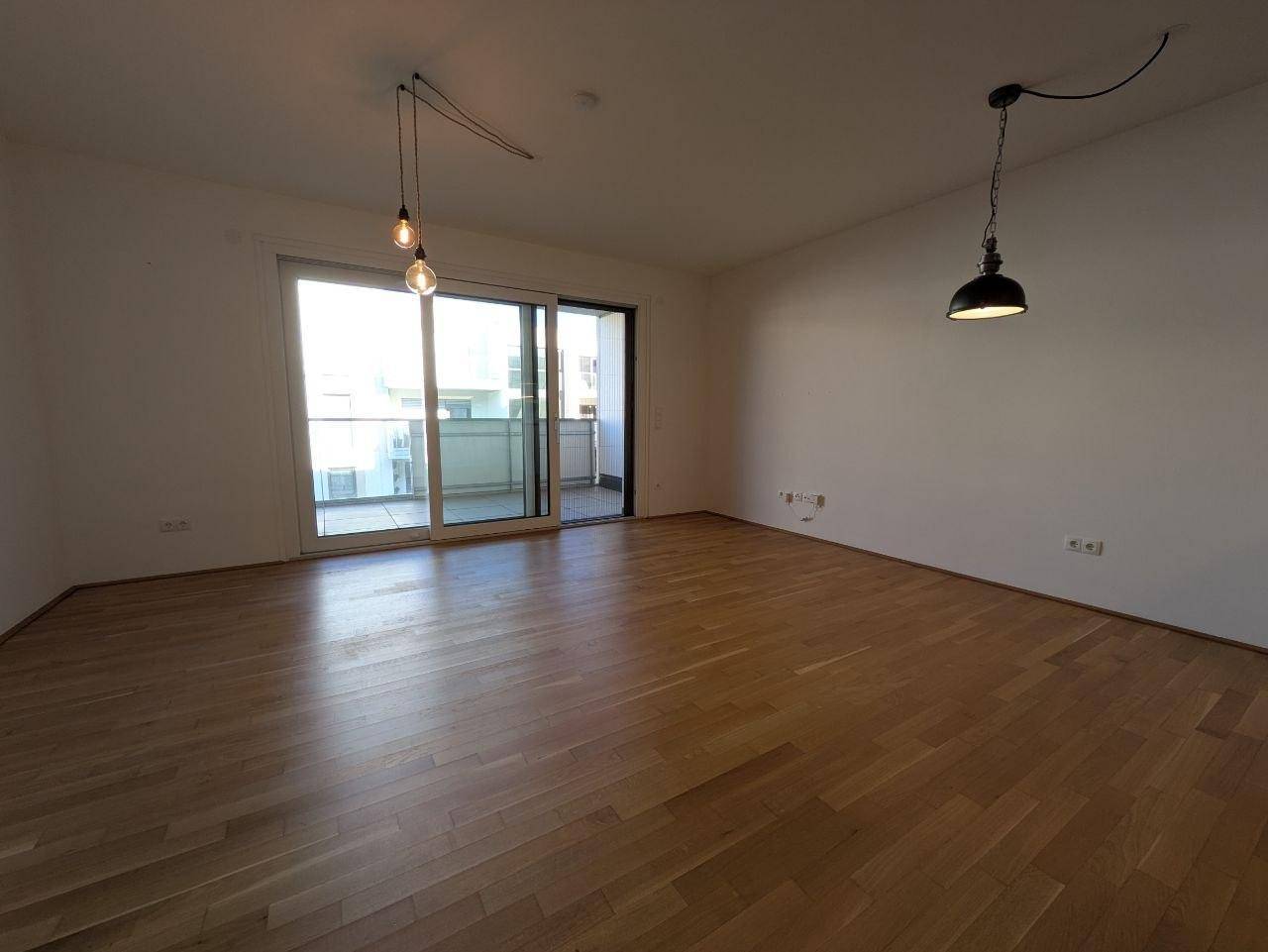 Heller Wohnbereich mit Zugang zum Balkon, Holzfußboden und modernen Leuchten.