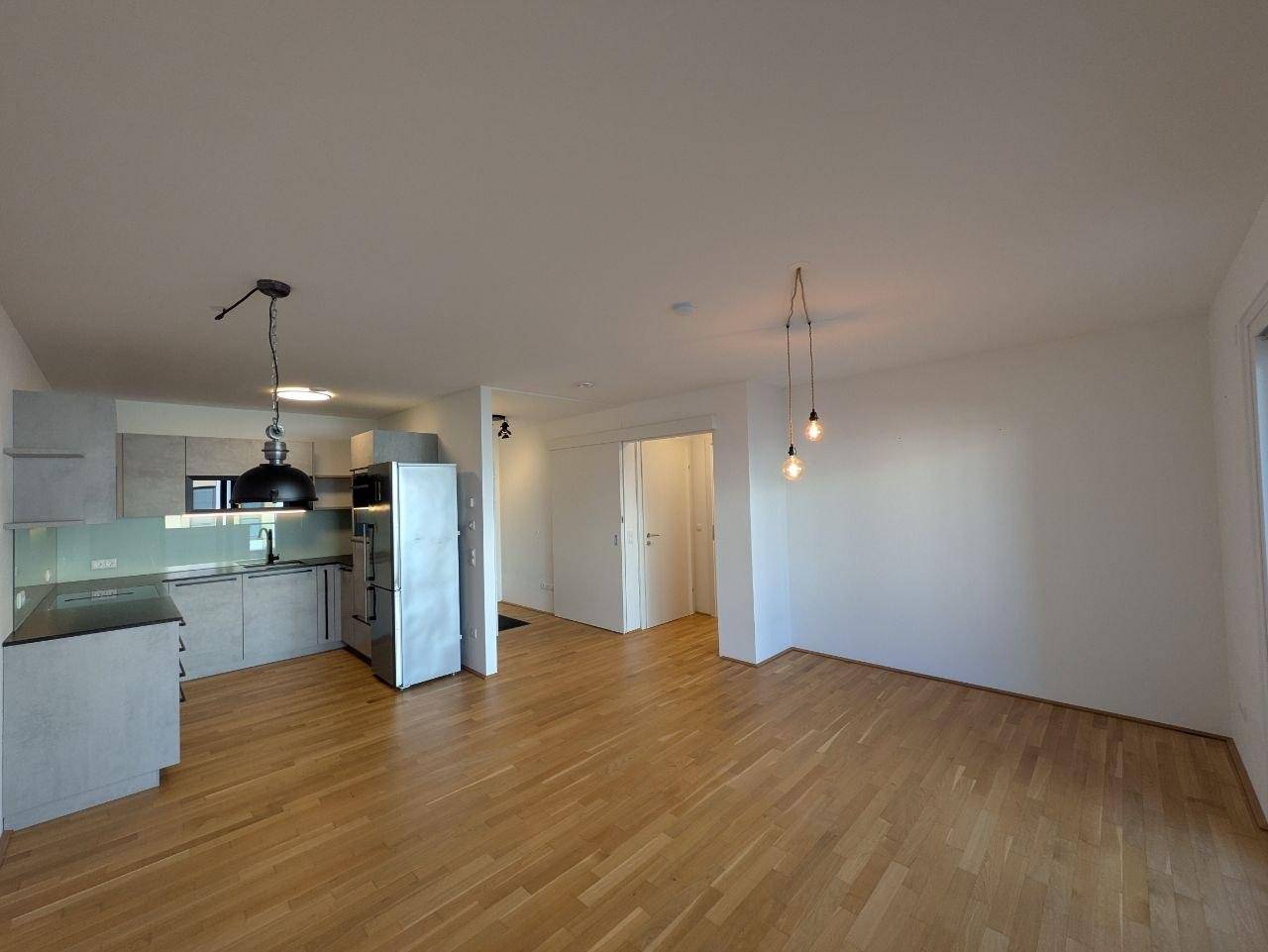 Offener Wohnbereich mit integrierter Küche, Holzfußboden und modernen Pendelleuchten.