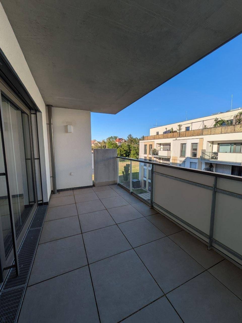 Geräumiger Balkon mit Fliesenboden und Glasbrüstung, bietet Ausblick auf die Umgebung.