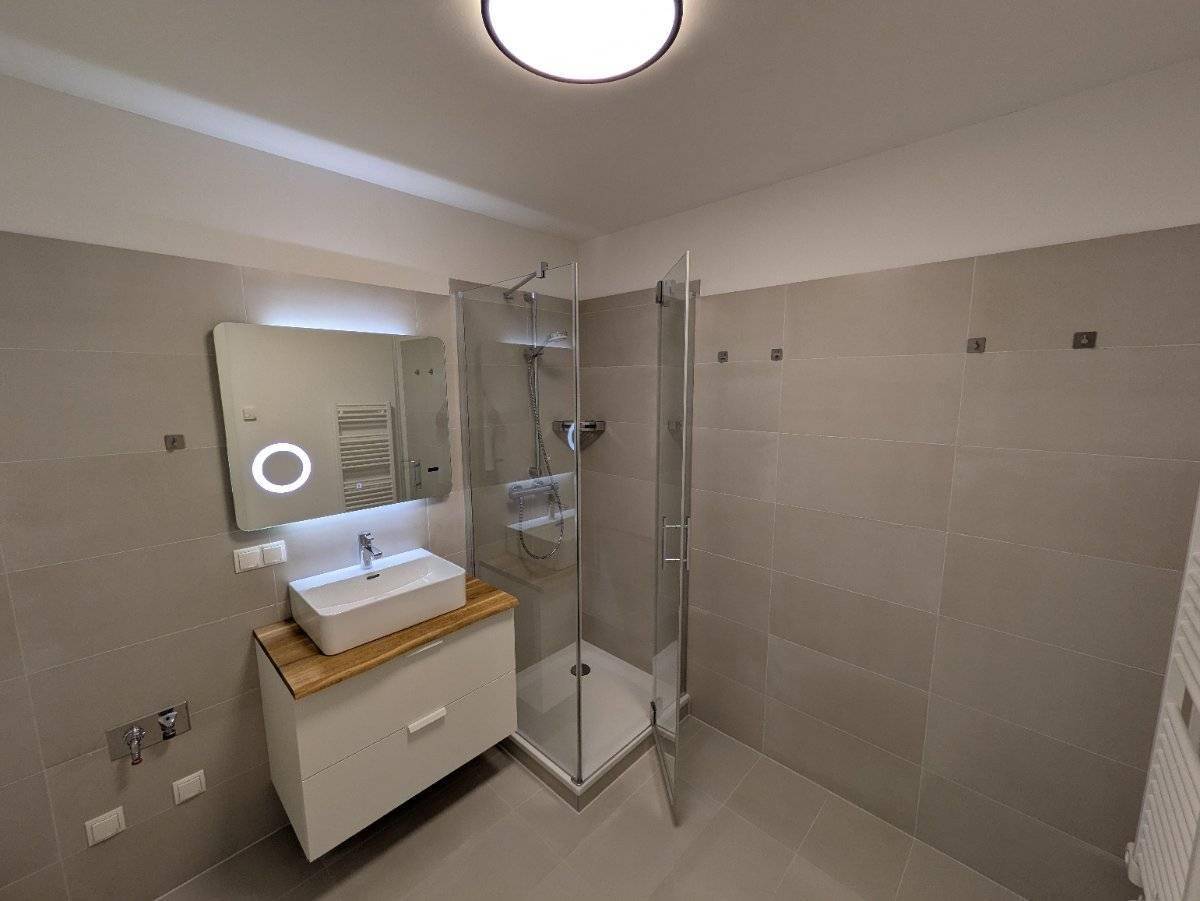 Modernes Badezimmer mit begehbarer Dusche, Waschtisch und beleuchtetem Spiegel.