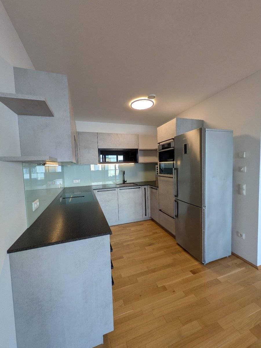Moderne Einbauküche mit grauen Fronten, dunkler Arbeitsplatte und Holzfußboden.